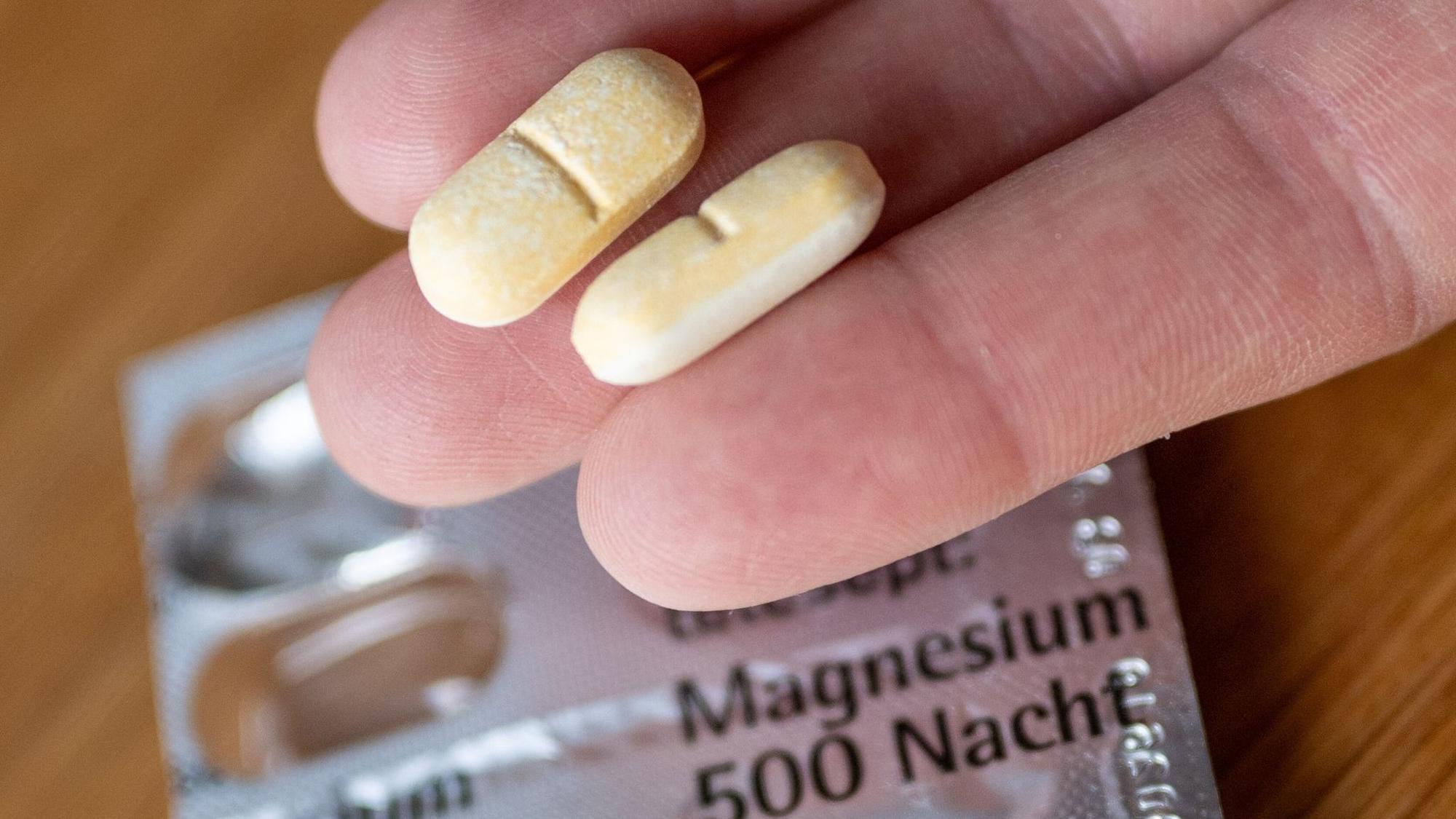 Ein Mann hält zwei Magnesium-Tabletten auf der Hand