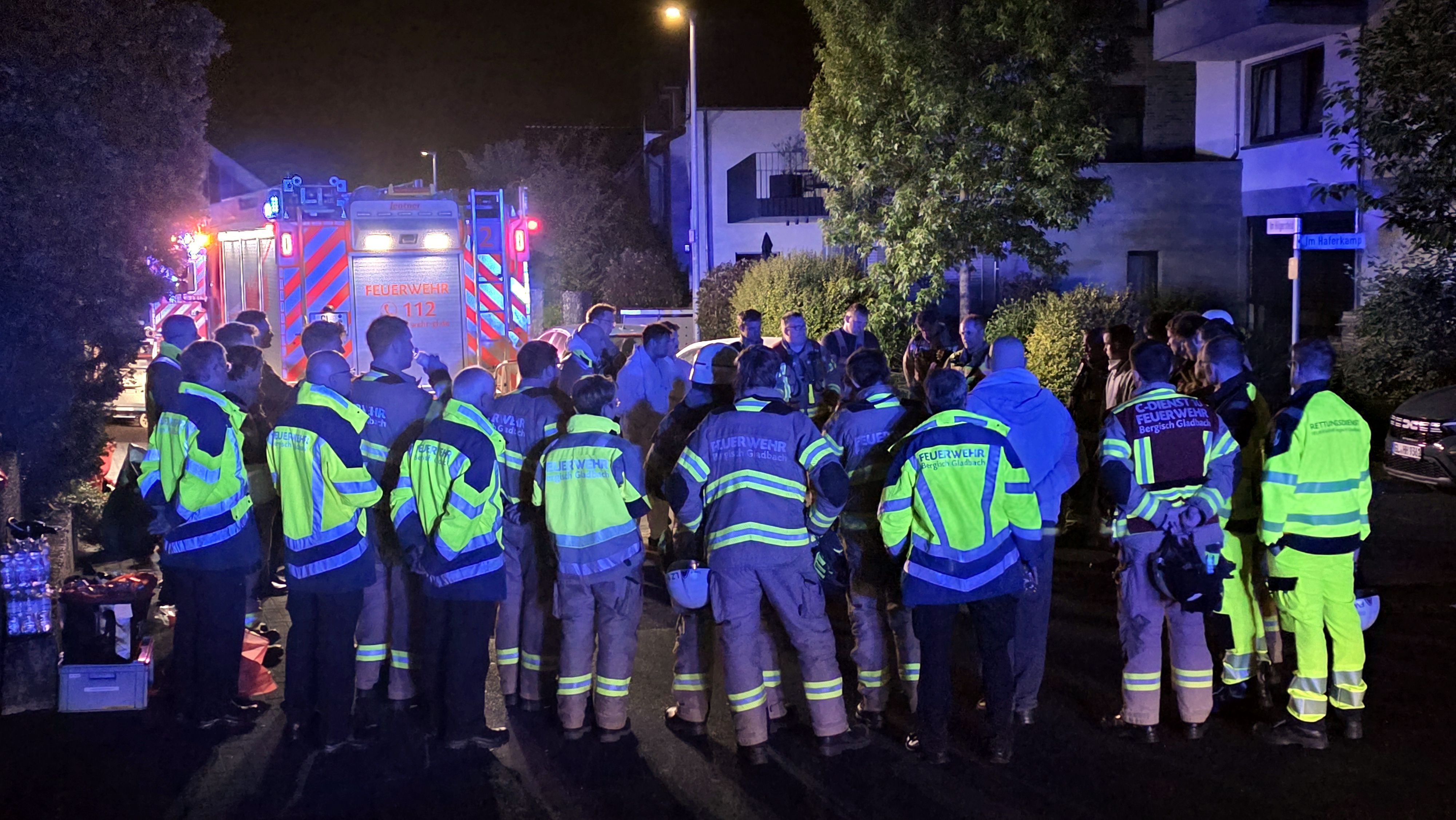 Feuerwehrleute stehen zur Nachbesprechung bei einem Wohnhausbrand auf einer Straße in Bergisch Gladbach-Lustheide.