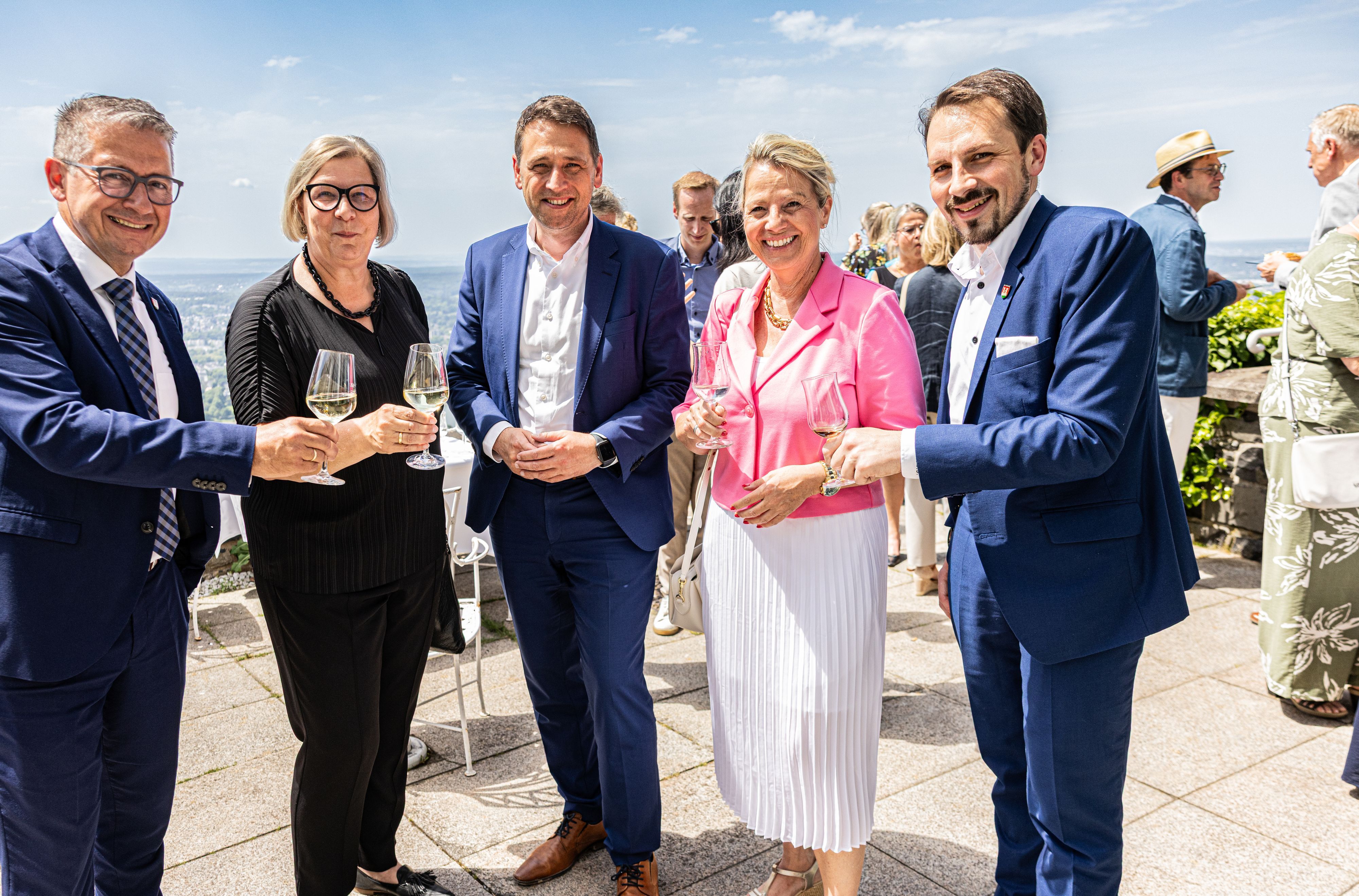 Männer und Frauen halten Gläser zum Prost in die Kamera.