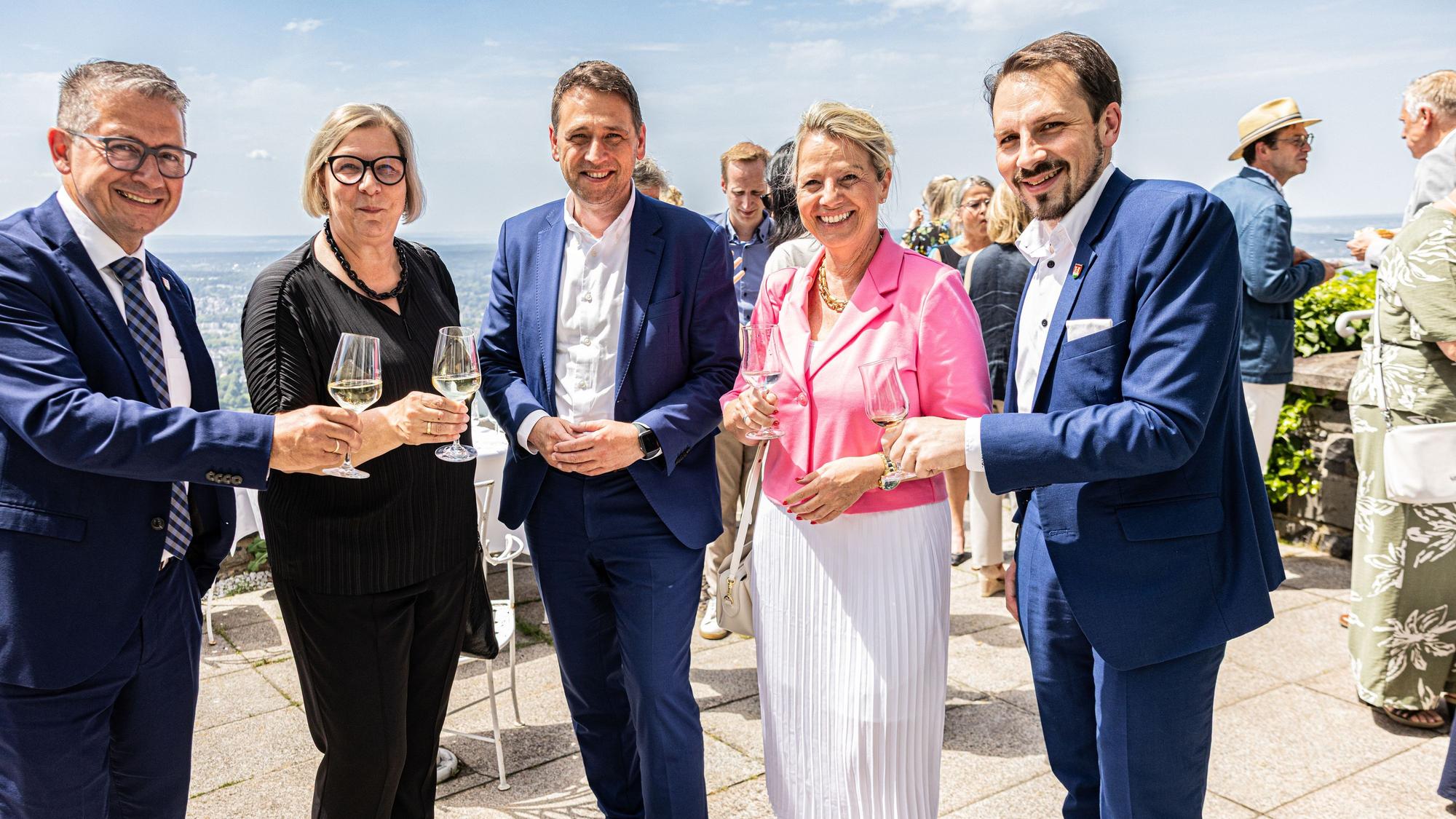 Männer und Frauen halten Gläser zum Prost in die Kamera.