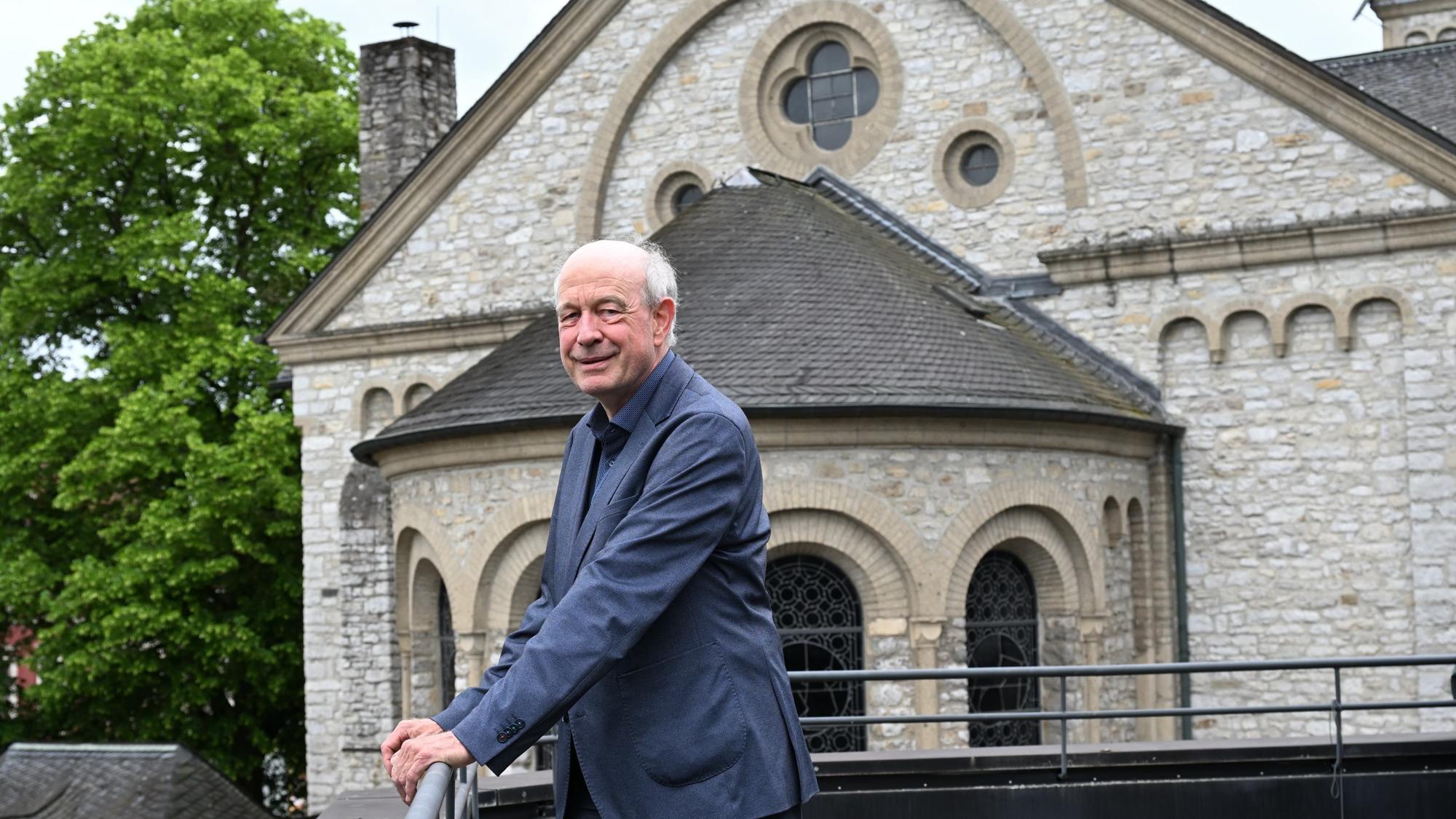 Ein Mann steht an einer Brüstung, dahinter sieht man die Apsis einer neoromanischen Kirche.