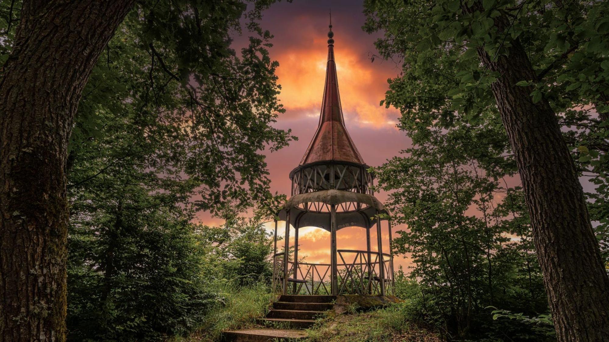Der Hohenzollernzurm bei Bad Bertrich in der Eifel ist vor einem in spektakulären Orangetönen gefärbten Himmel zu sehen.