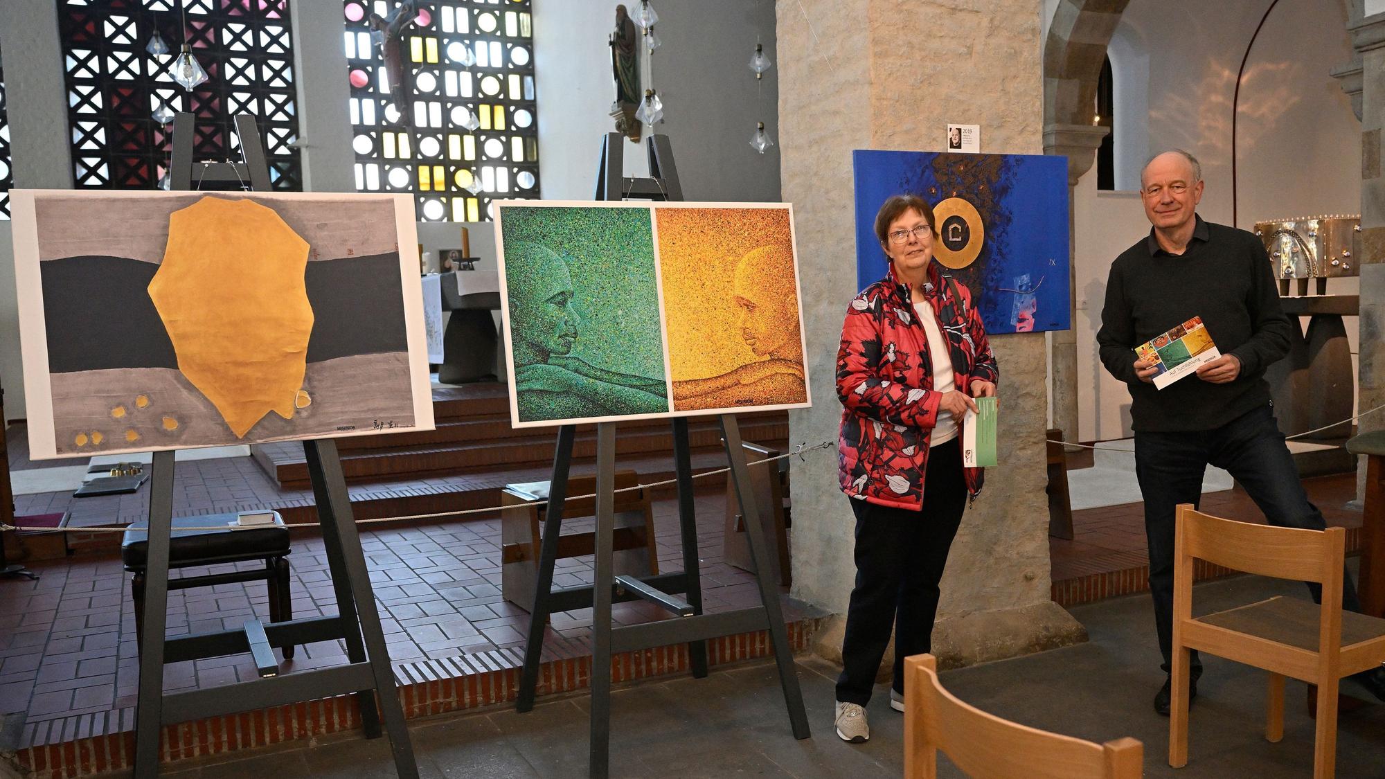 Bilder von Hunger- oder Fastentüchern werden in einer Kirche ausgestellt. Daneben stehen ein Mann und eine Frau.