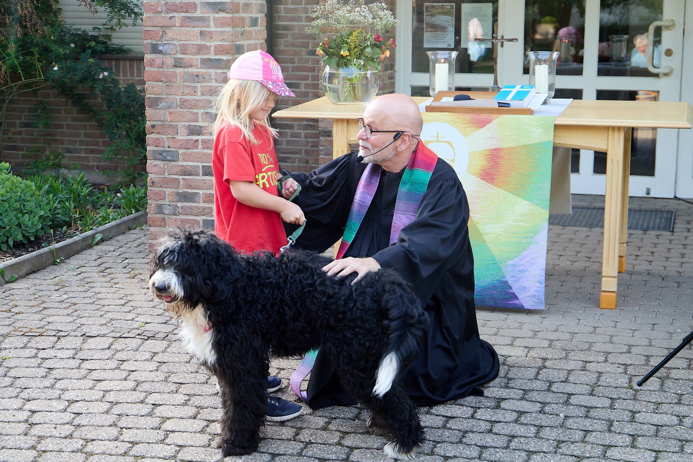 Ein Kind und ein Hund stehen neben einem knieenden Geistlichen.