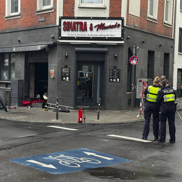 Blick auf die beschädigte Bar "Sinatra & Monroe's" mit eingeschlagener Scheibe, Trümmern auf dem Boden und einem Feuerlöscher davor. Im Vordergrund stehen zwei Polizeibeamte mit Warnwesten an einem abgesperrten Bereich. Friesenwall, Köln