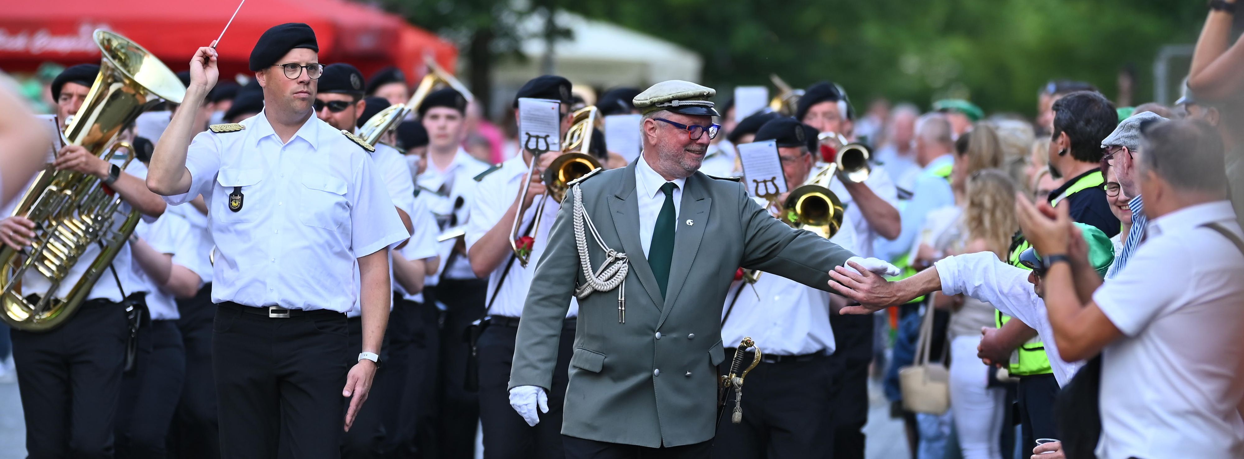 Ein Mann in Schützenuniform begrüßt einen Passanten.