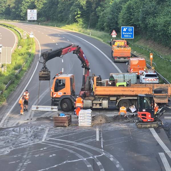 Ein großer Lkw quer auf der Fahrbahn, davor Bauarbeiter.