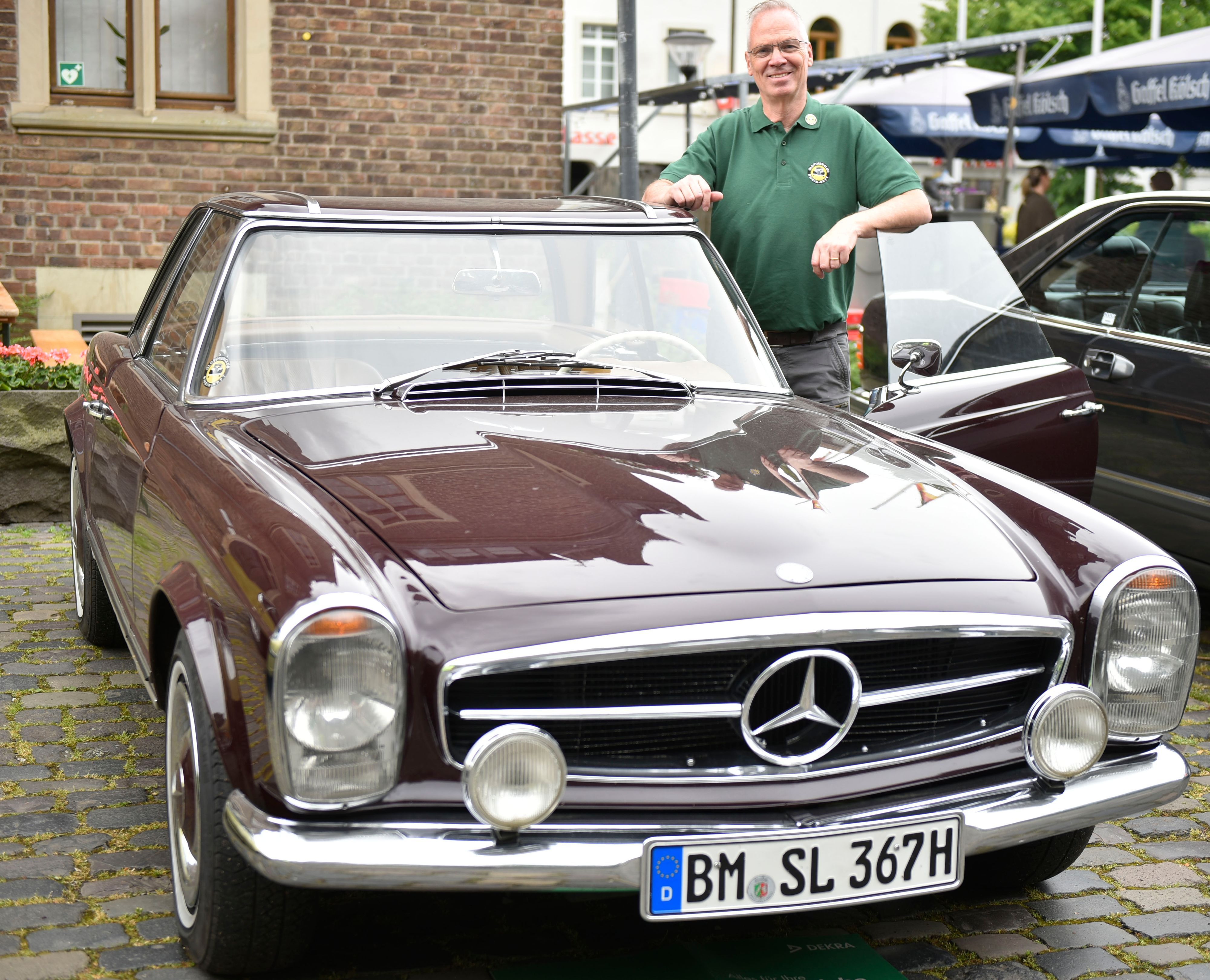 Ein Mann steht in der geöffneten Tür seiens dunkelroten Mercedes 250 SC von 1967.