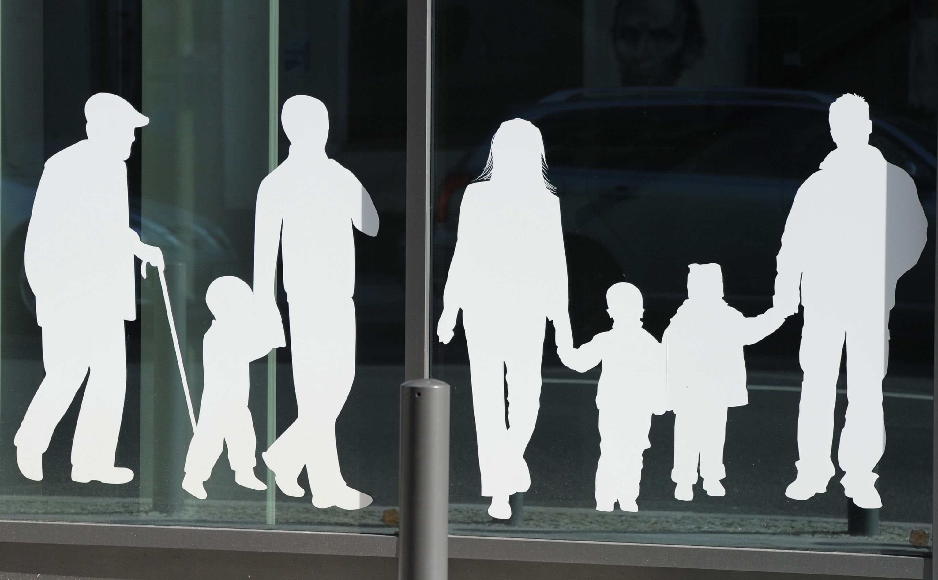 Figuren von Menschen in verschiedenem Alter sind auf Fensterscheiben aufgeklebt. 2025 sind weniger Menschen nach Deutschland gezogen. (Symbolbild)