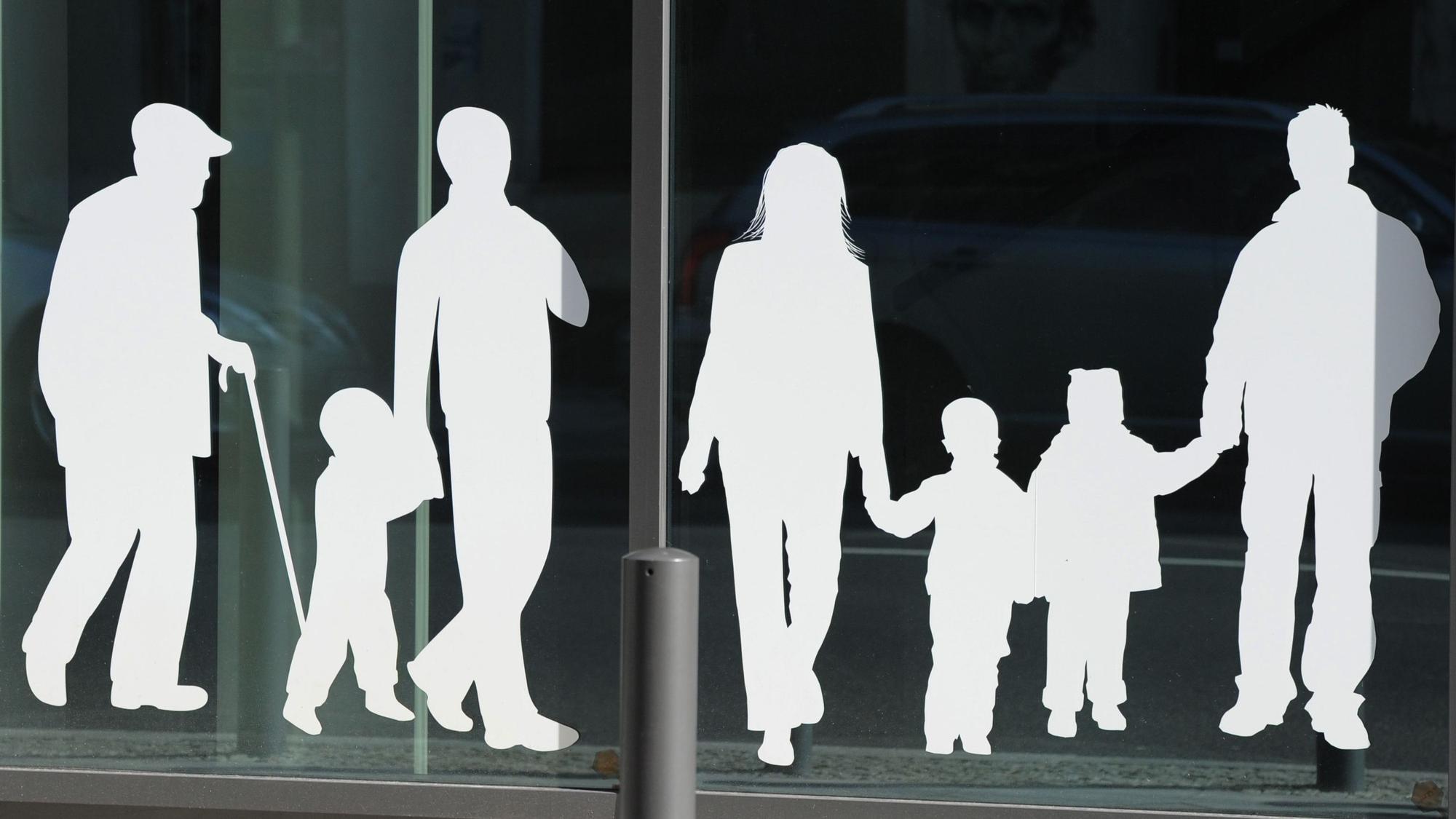 Figuren von Menschen in verschiedenem Alter sind auf Fensterscheiben aufgeklebt. 2025 sind weniger Menschen nach Deutschland gezogen. (Symbolbild)