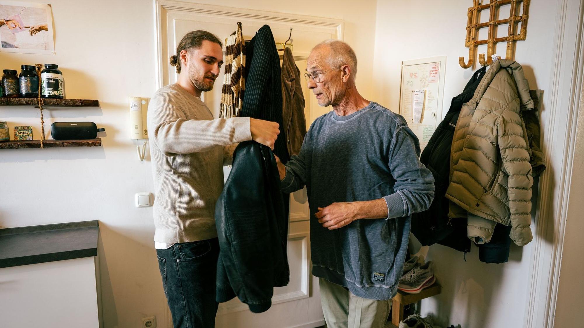 Ein junger Mann hilft einem Senior die Jacke anzuziehen