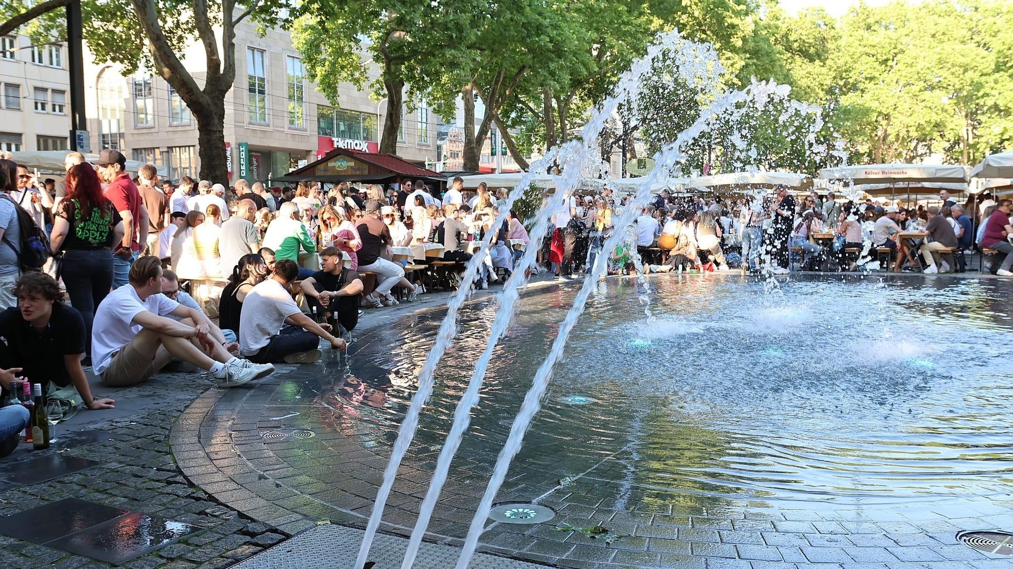 Eine Menschenmenge sitzt um den Brunnen auf dem Neumarkt.