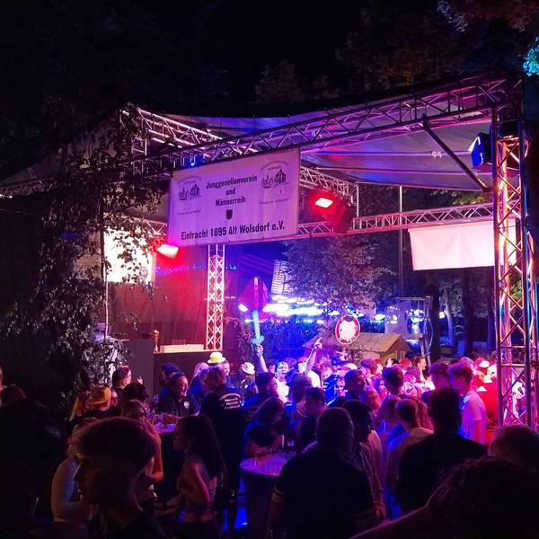 Eine Menschenmenge feiert im Partylicht vor einer Bühne.