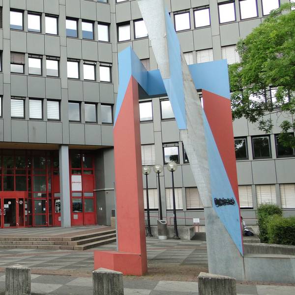 Die Zweigstelle des Jobcenters Chorweiler, ein graues mehrgeschossiges Gebäude mit rotem Eingangsbereich.