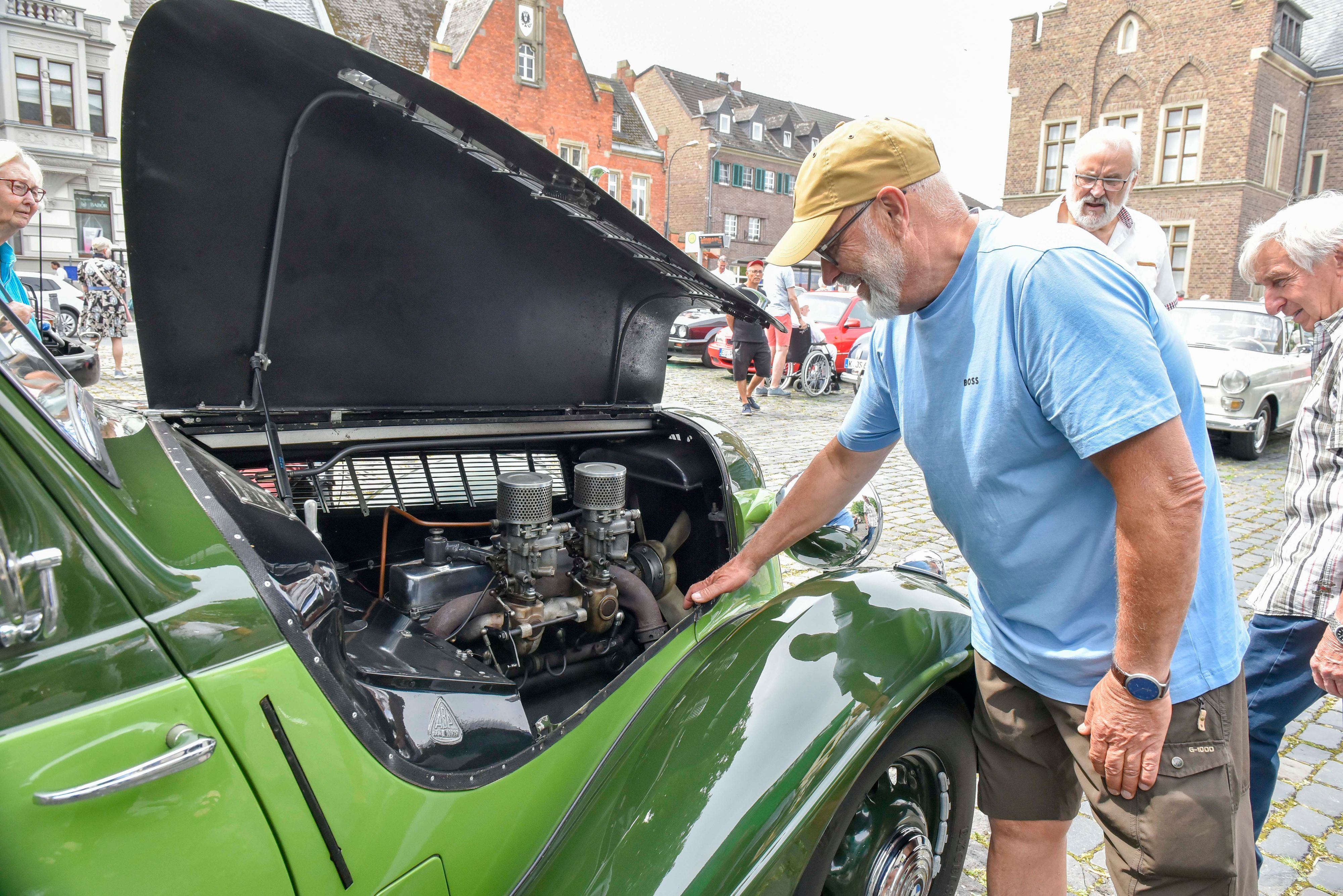 Ein Mann schaut in die Motorhaube eines Oldtimers.