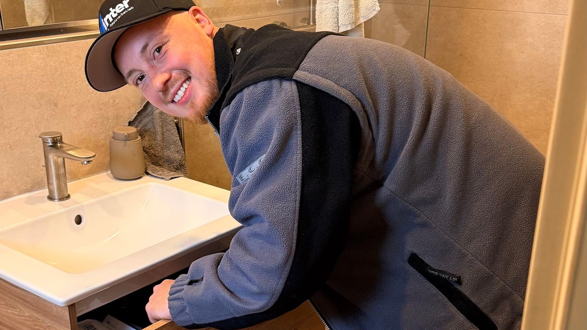 Ein junger Mann schaut in die Kamera, er beugt sich über ein Waschbecken.