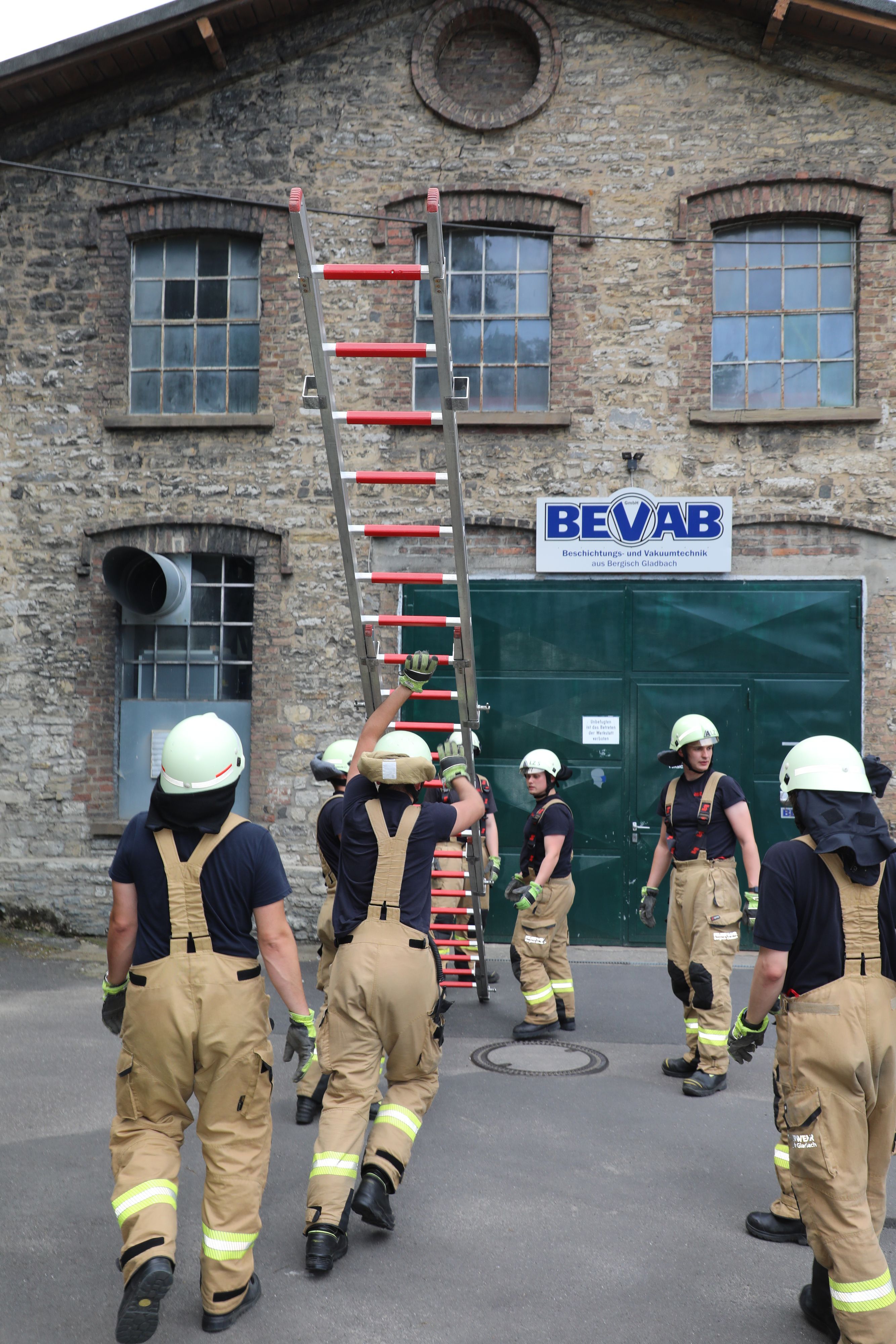 Feuerwehrleute vor einer Hauswand, die eine Leiter hochstemmen.
