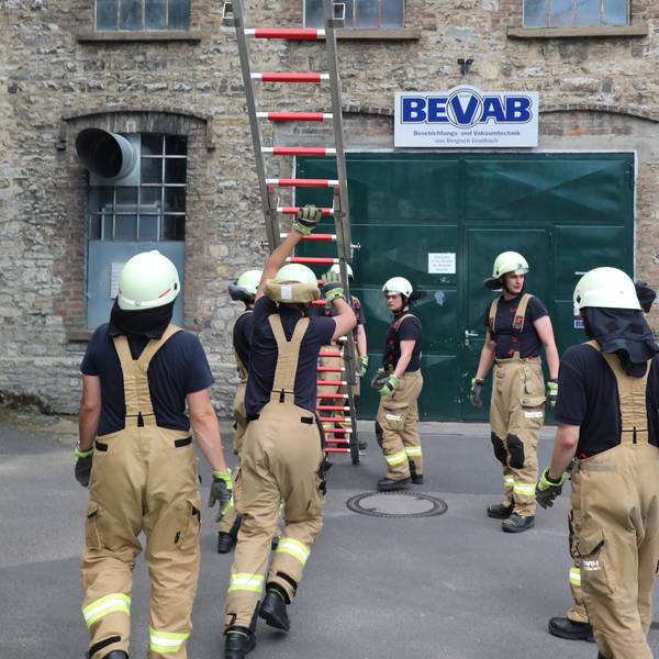 Feuerwehrleute vor einer Hauswand, die eine Leiter hochstemmen.