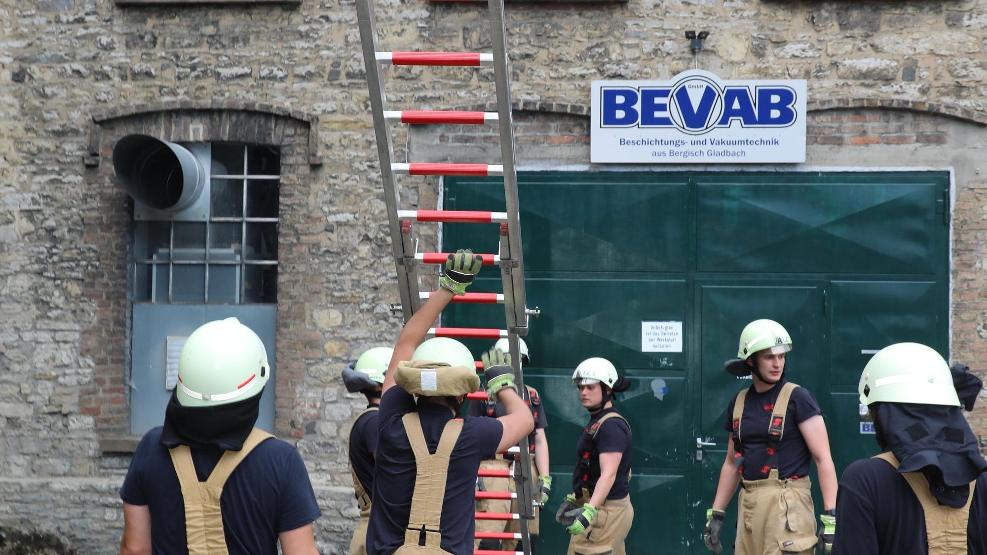 Feuerwehrleute vor einer Hauswand, die eine Leiter hochstemmen.