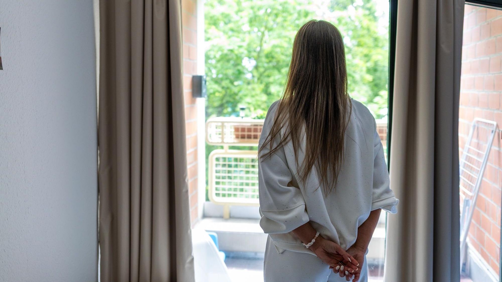 Eine Frau von hinten abgebildet vor einem Fenster.