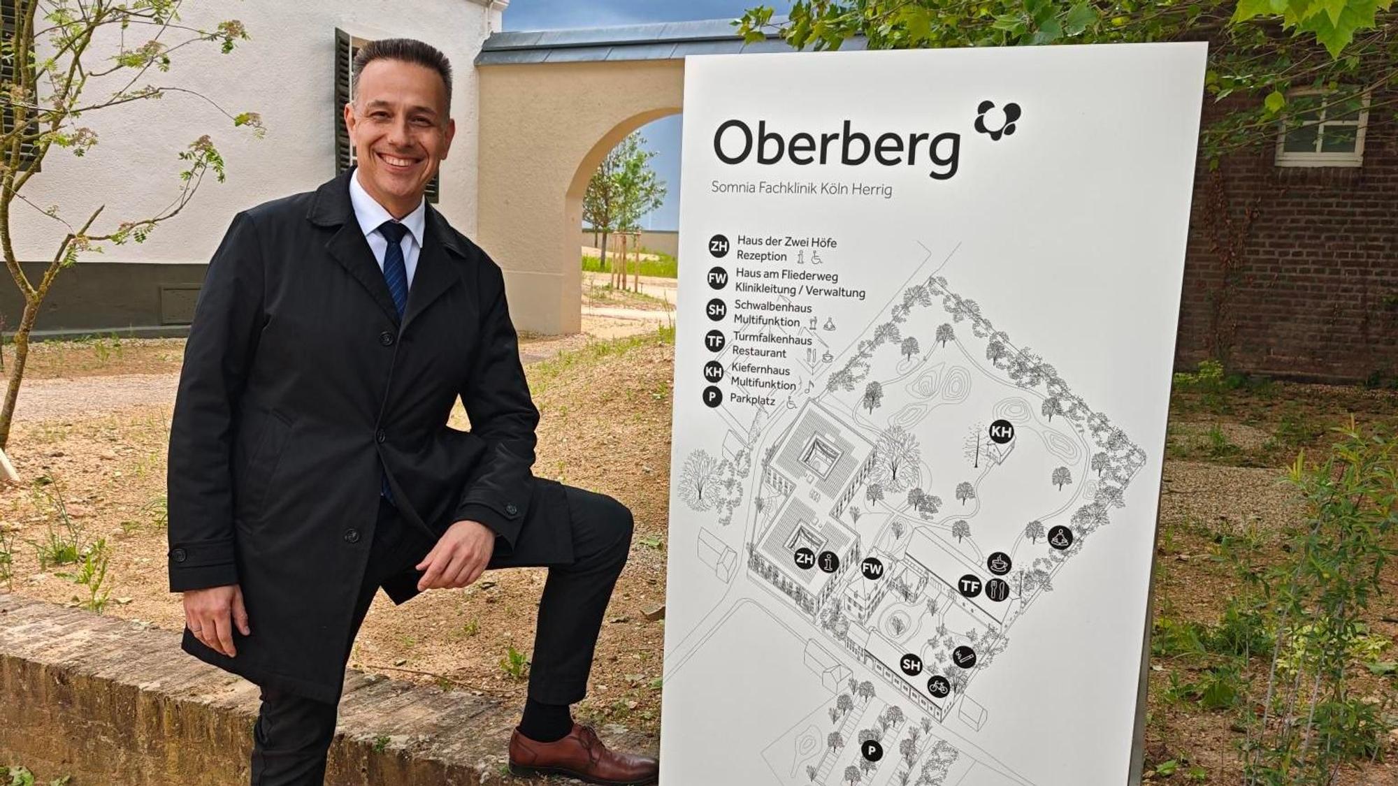 Ein Mann im Anzug steht neben einem Schild.
