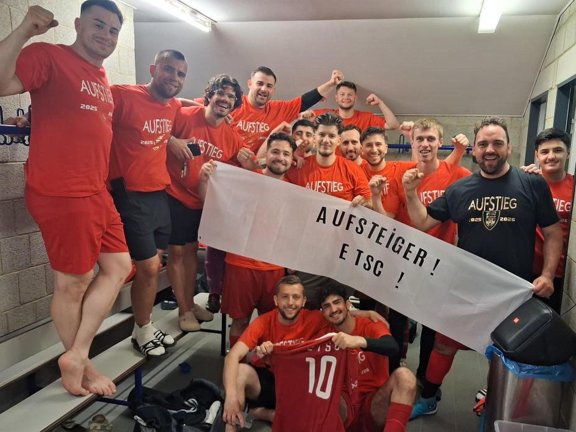 Die Mannschaft des Euskirchener TSC freut sich in der Kabine über den Aufstieg. Die Spieler halten ein Transparent mit der Aufschrift "Aufsteiger! ETSC!" hoch.