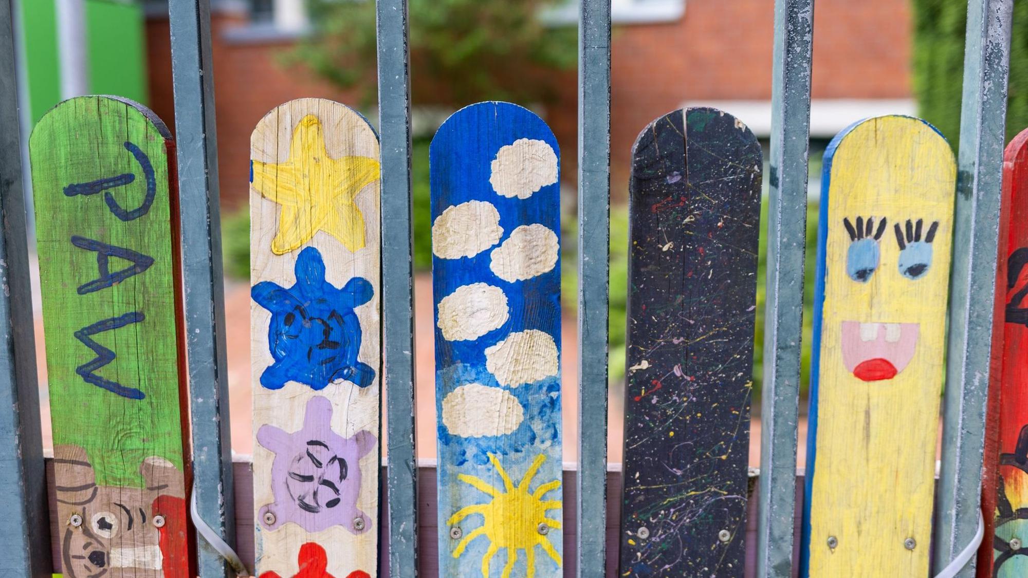 Ein grauer Zaun mit bunt angestrichenen Holzbalken.