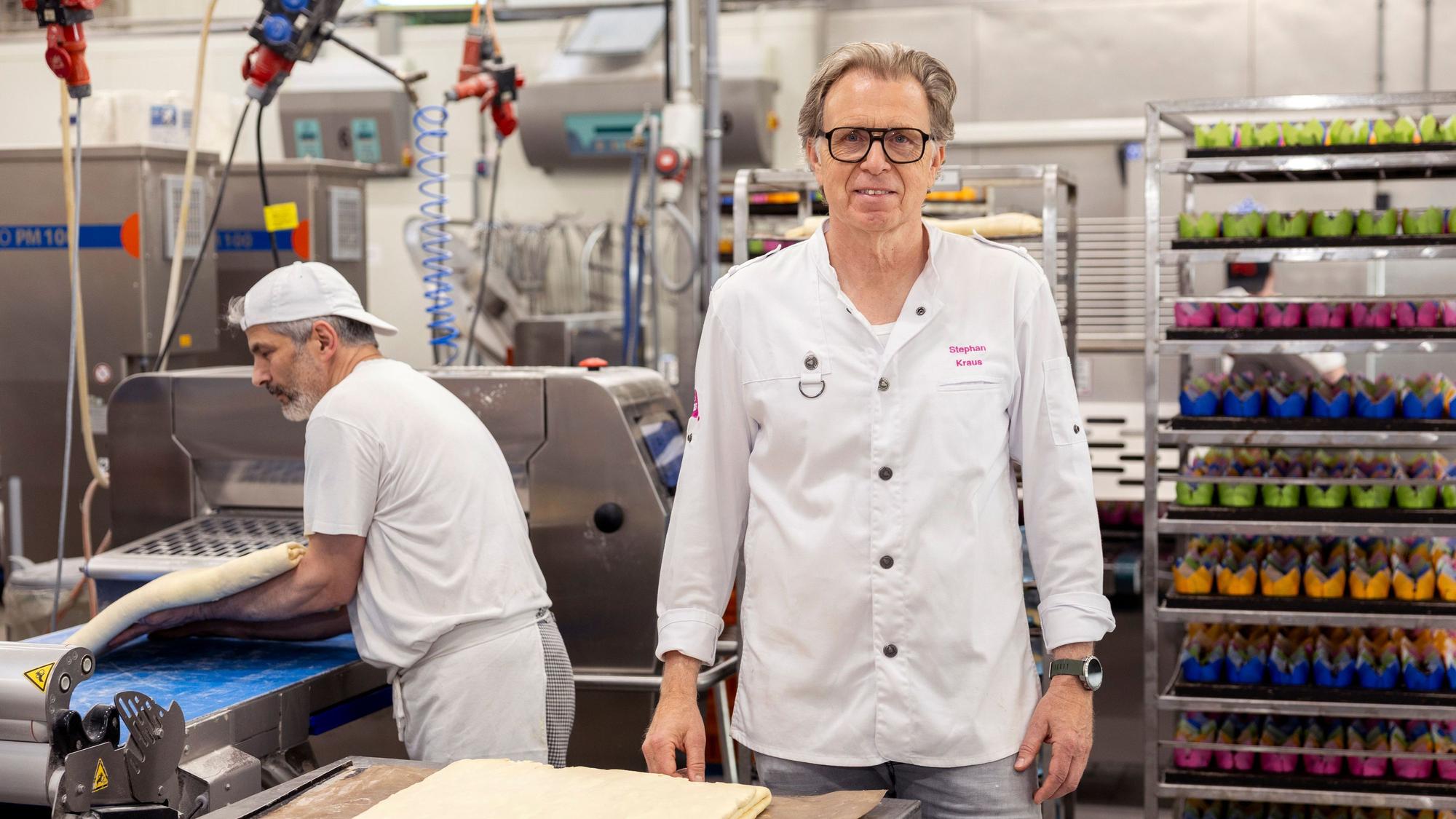 Stephan Kraus steht in der Produktionshalle der Bäckerei Kraus. Hinter ihm hievt ein Mitarbeiter Teig auf ein Band.