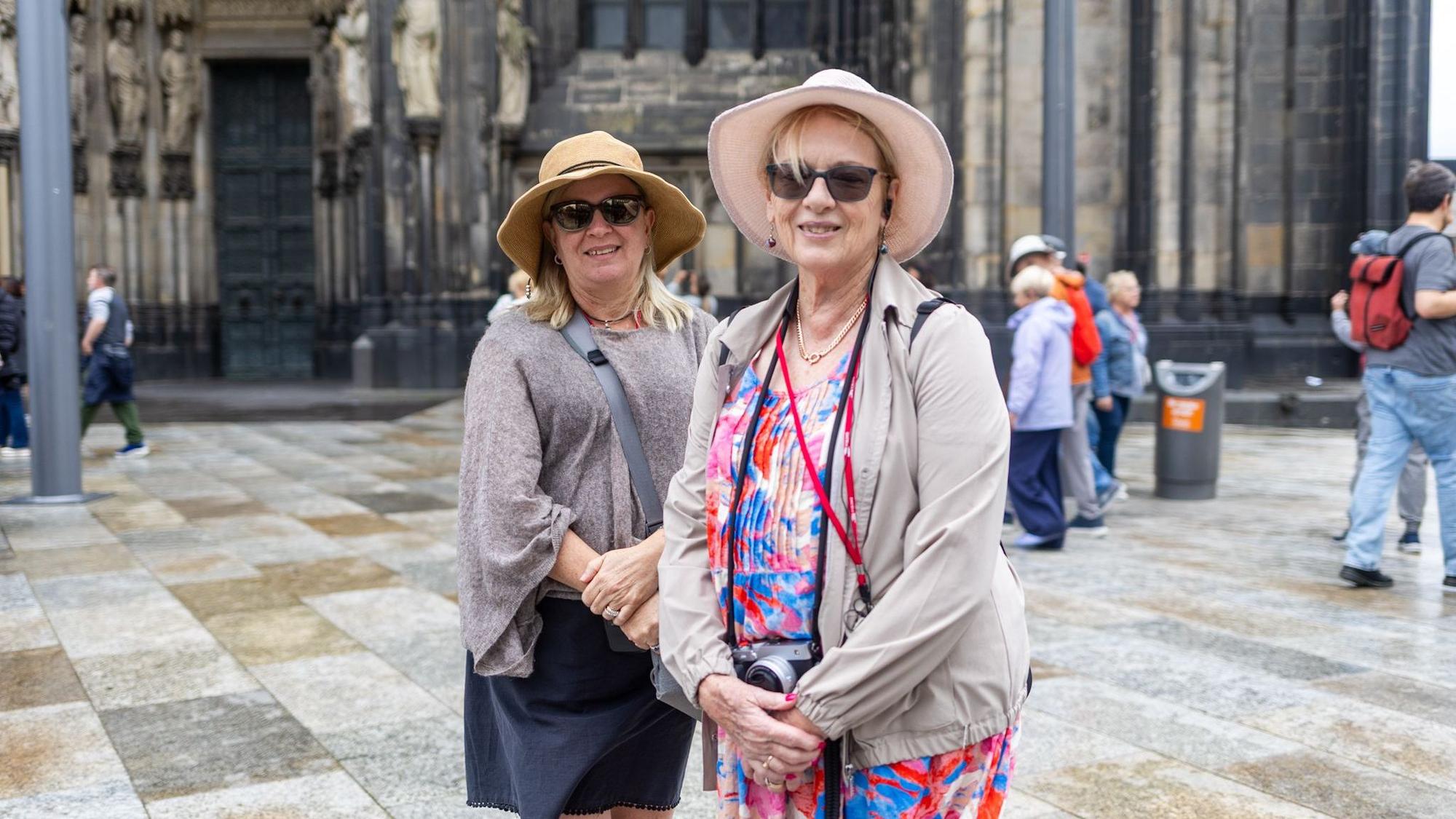 Zwei Frauen mit Sonnenhut und Brille stehen vor dem Dom.