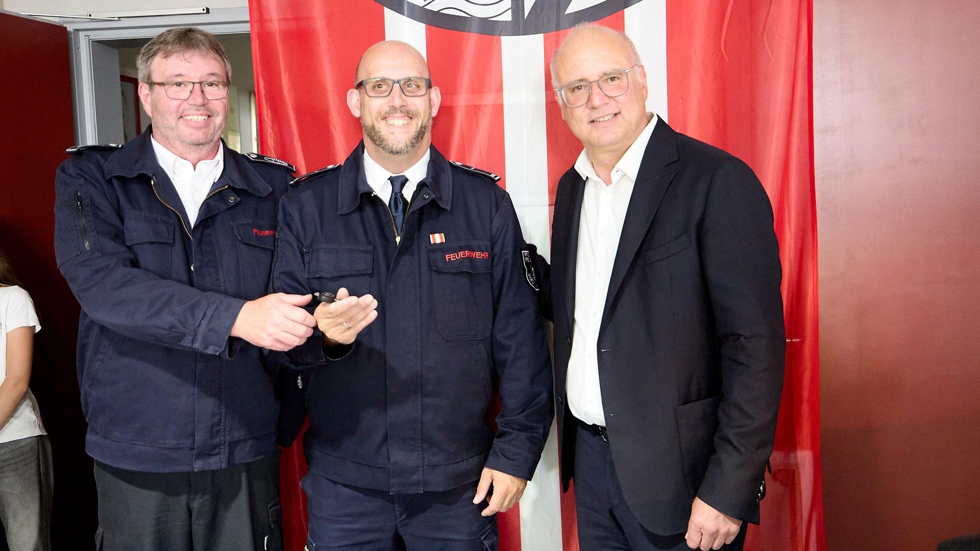Die drei Männer stehen vor einer Fahne der Feuerwehr.