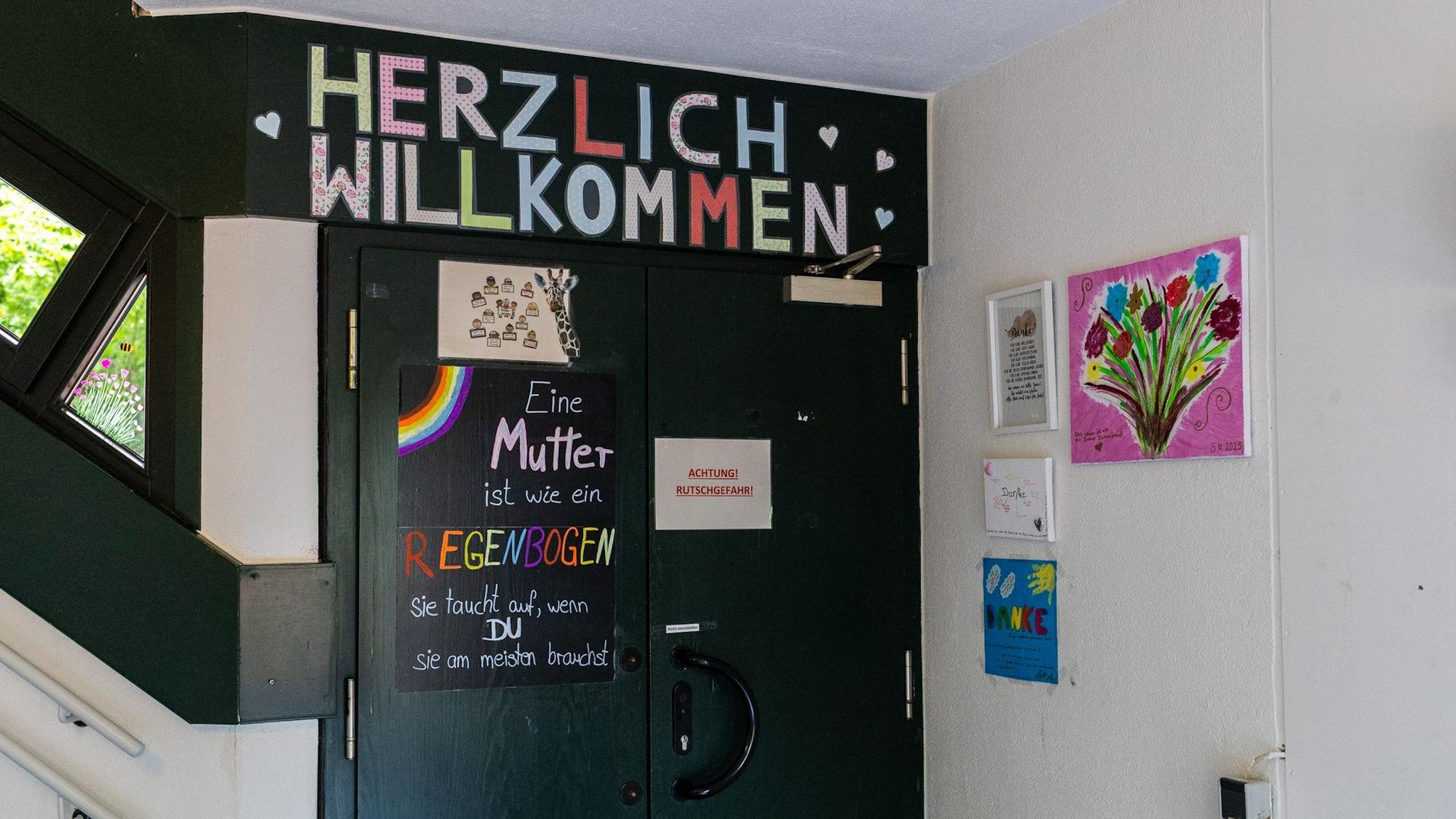 Tür mit „Herzlich Willkommen“, daneben hängen Bilder mit Blumen.