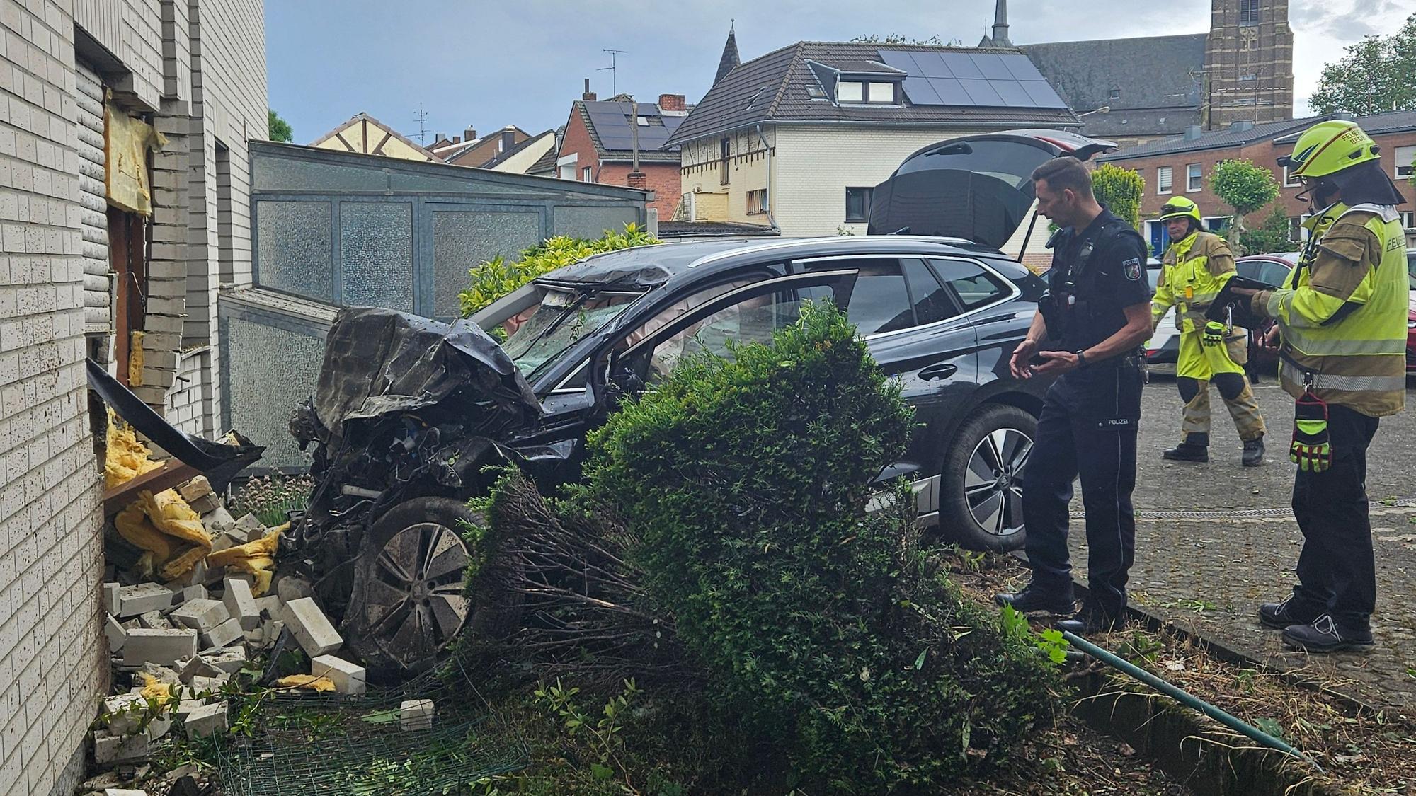 Das Bild zeigt ein Auto an einer Hauswand und Einsatzkräfte.