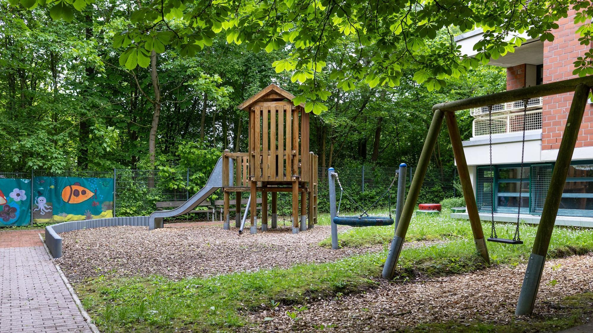 Blick auf den Garten: Ein Spielhaus mit Rutsche und Schaukeln.