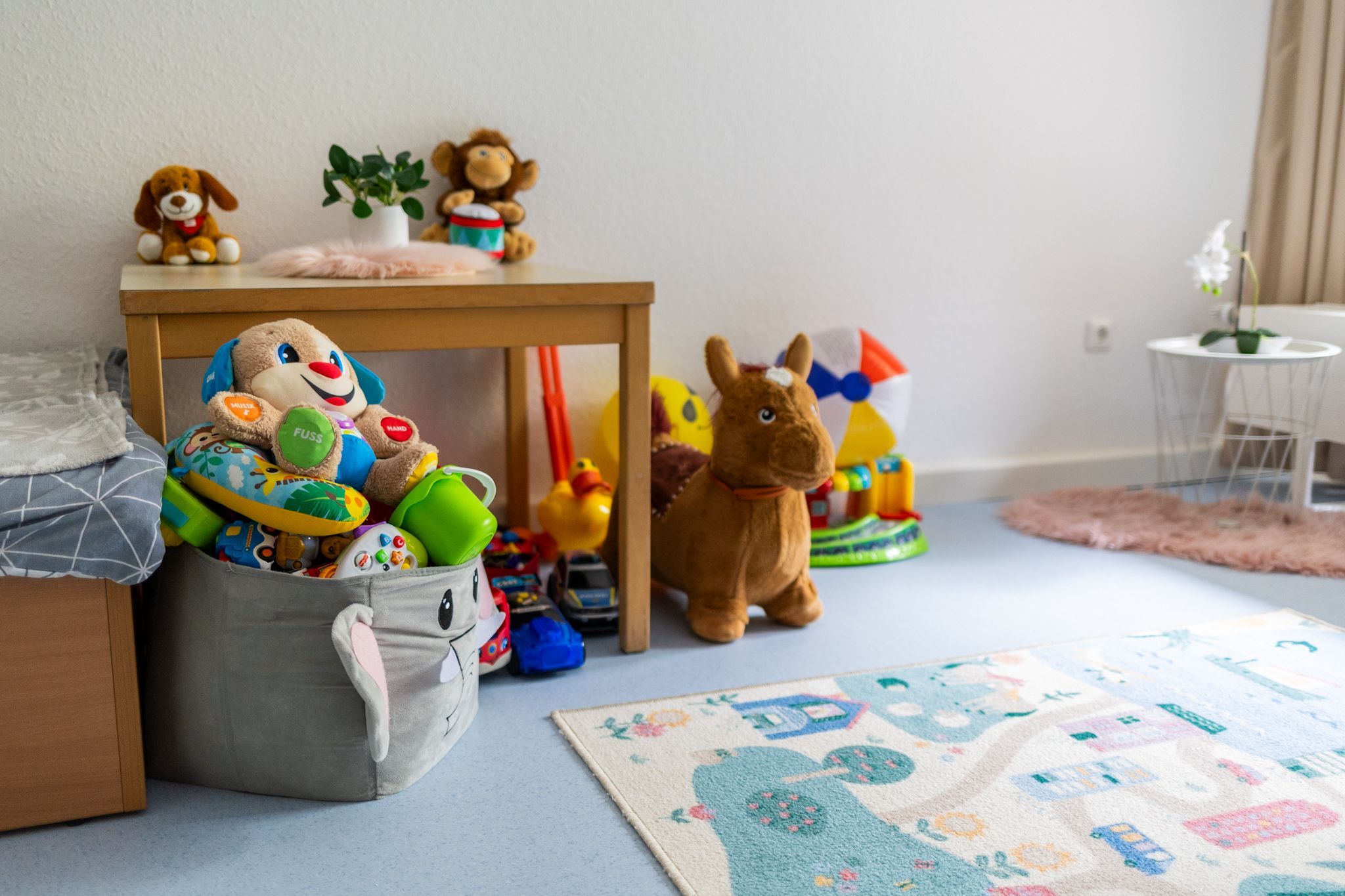 Stofftiere liegen in einer Kiste, daneben liegt ein Spielteppich.