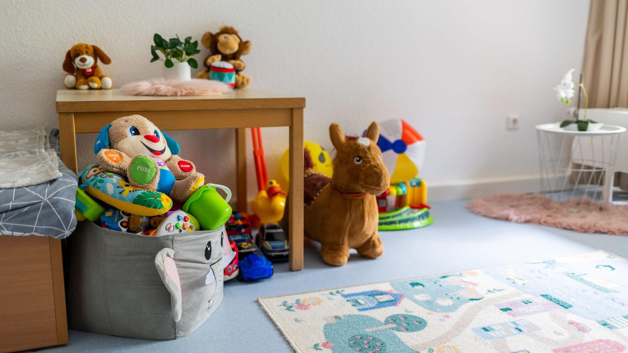 Stofftiere liegen in einer Kiste, daneben liegt ein Spielteppich.