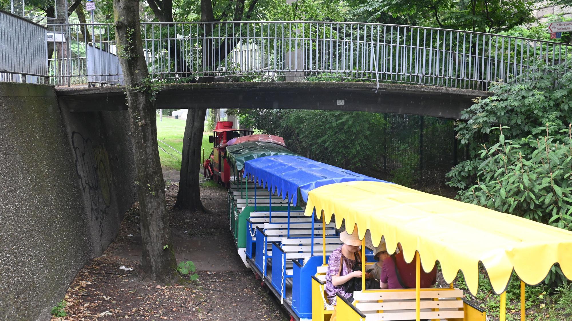 02.06.2026 Köln. Im Rheinpark führt eine kleine Brücke an der Fußgängerampe zur Zoobrücke über die Gleise der dortigen Kleinbahn, die hier ihre Haltestelle „Rosengarten“ hat. Die Parkeisenbahn wurde zur Bundesgartenschau 1971 errichtet. Foto: Alexander Schwaiger