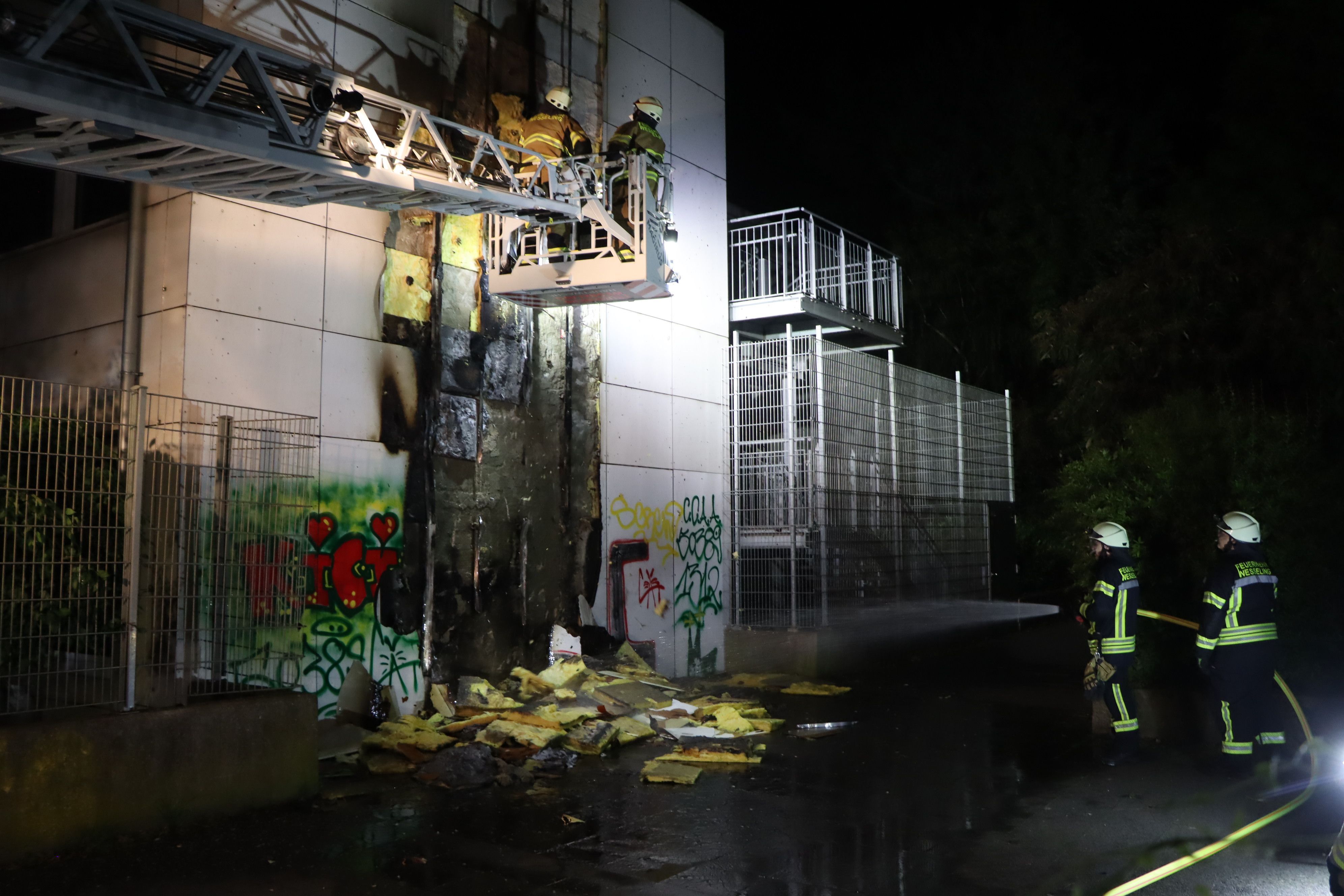Zu sehen sind Feuerwehrleute vor der vom Feuer beschädigten Fassade.