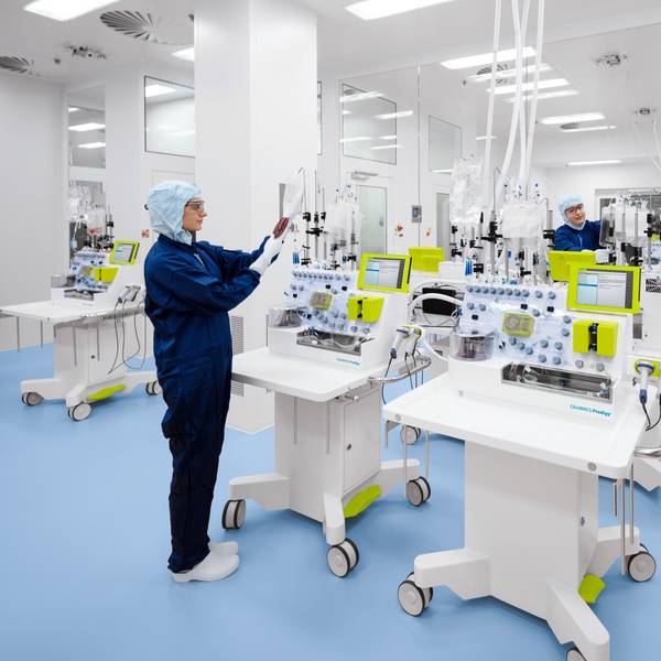 Eine Mitarbeiterin in einem blauen Overall arbeitet an weißen Laborgeräten in einem Reinraum.