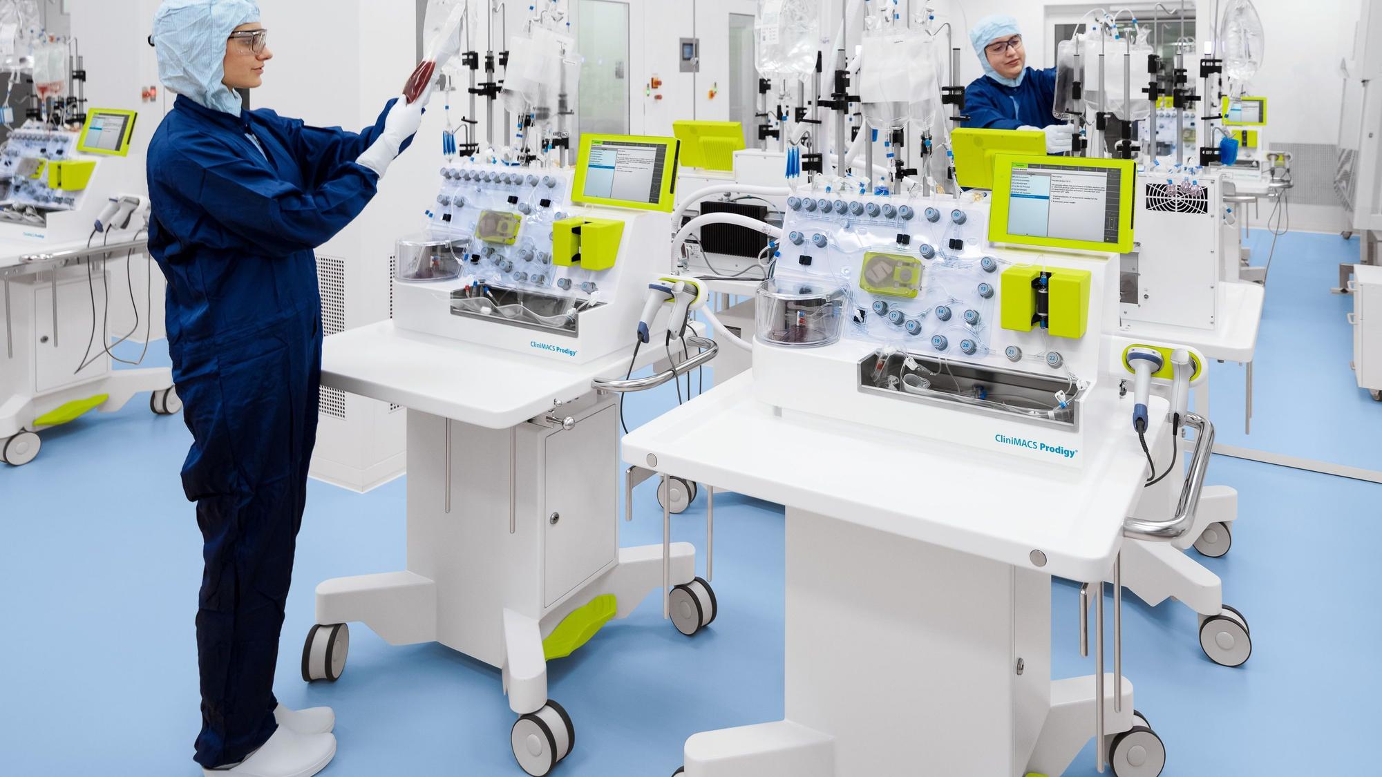 Eine Mitarbeiterin in einem blauen Overall arbeitet an weißen Laborgeräten in einem Reinraum.