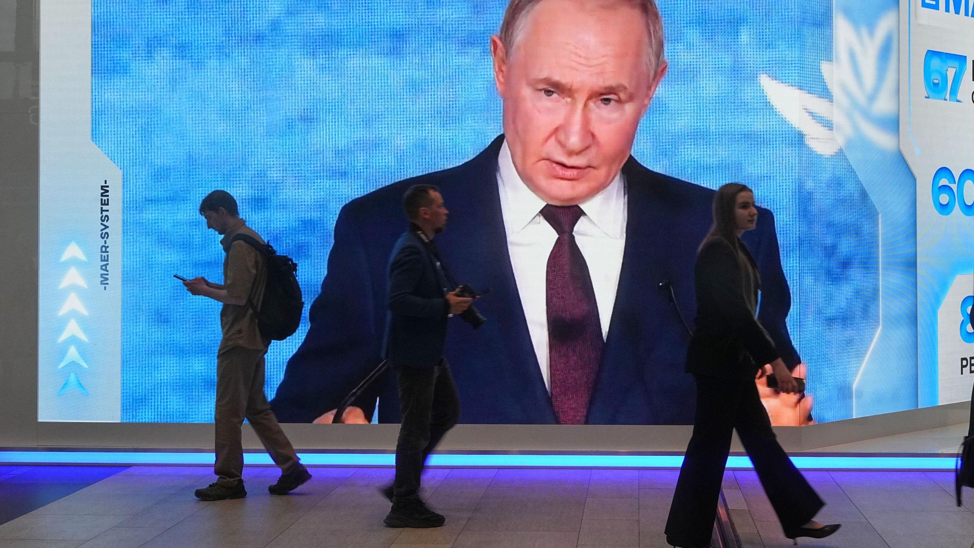 Menschen gehen an einem Bildschirm mit einem Bild des russischen Präsidenten Wladimir Putin auf dem Internationalen Wirtschaftsforum in St. Petersburg vorbei.