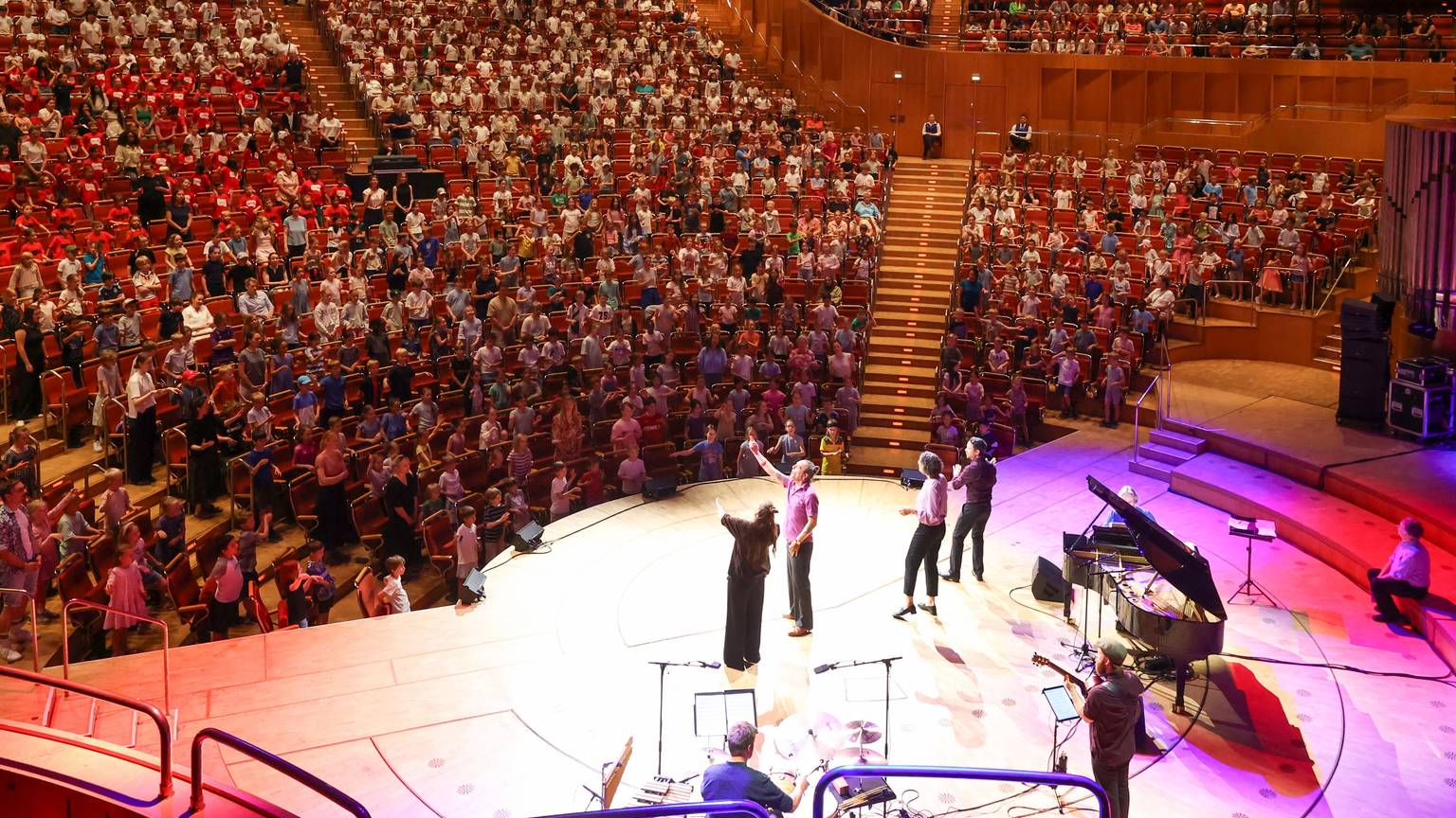 1.000 Kölner Grundschülerinnen und -schüler sitzen in den Rängen der Kölner Philharmonie und singen, auf der Bühne stehen vier Singleiterinnen.