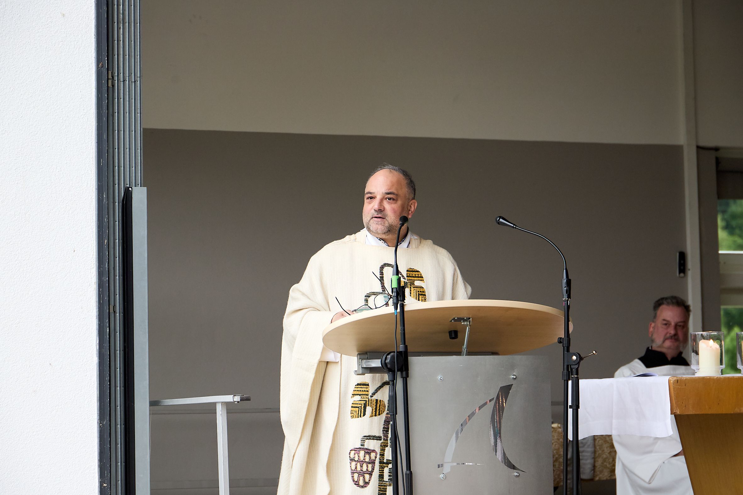 Ein Mann mit kurzen Haaren steht im Priester-Gewand an einem Ambo.