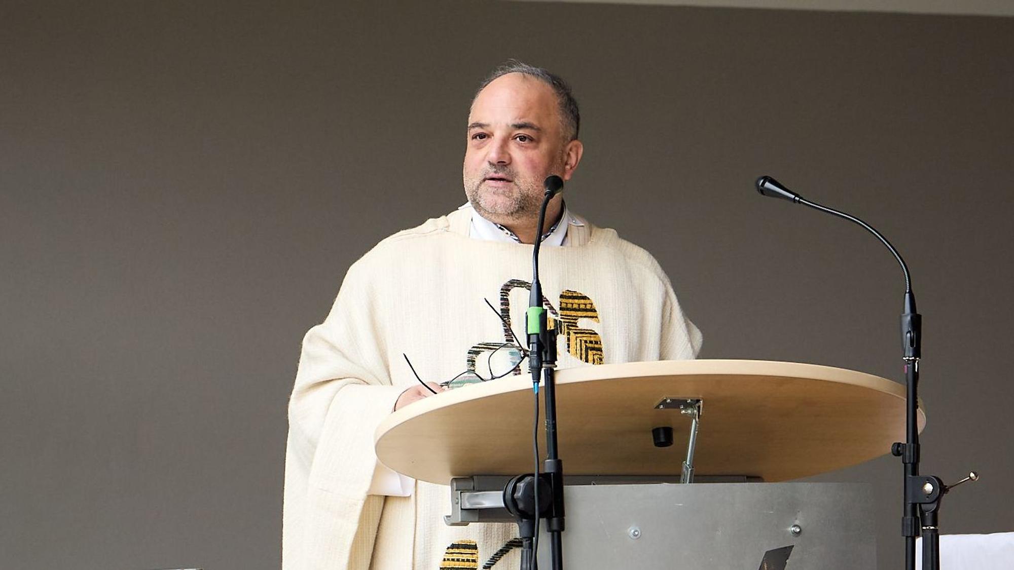 Ein Mann mit kurzen Haaren steht im Priester-Gewand an einem Ambo.
