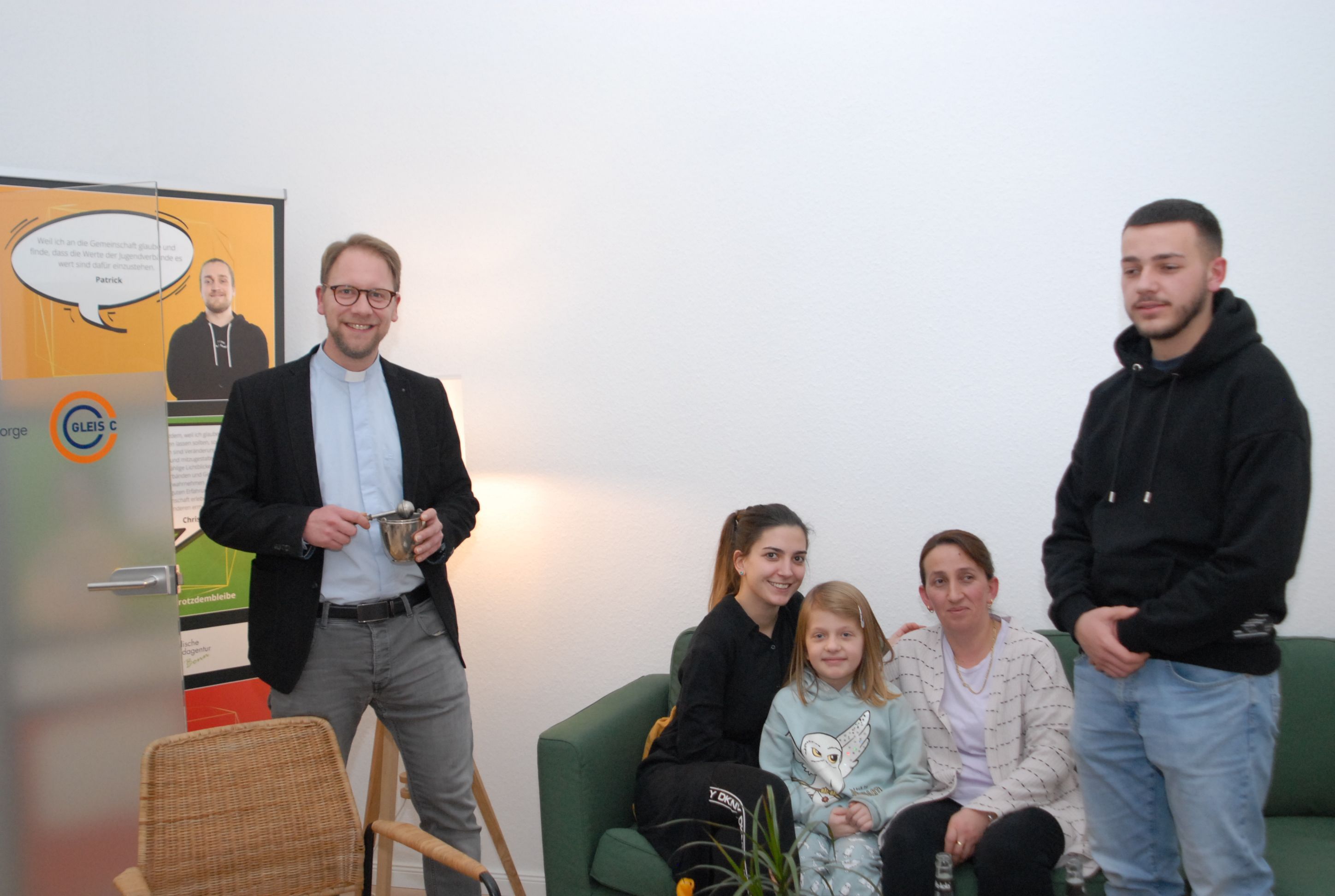 Tobias Schwaderlapp hält die Utensilien für eine Segnung in Händen, er steht vor einem Plakat.