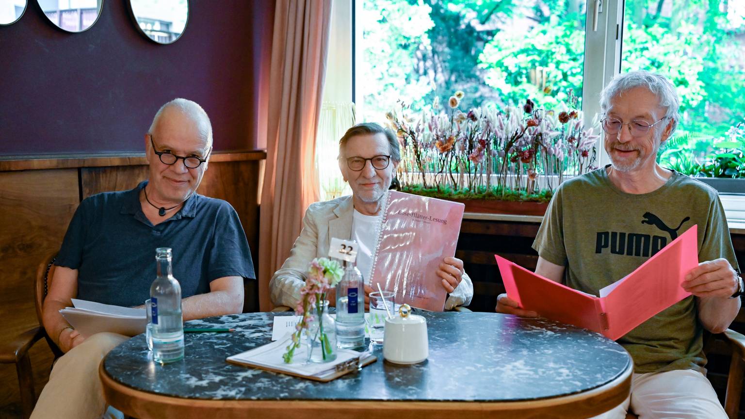 Drei Männer sitzen mit ihren Texten an einem Tisch im Café Osterspey in Sülz.