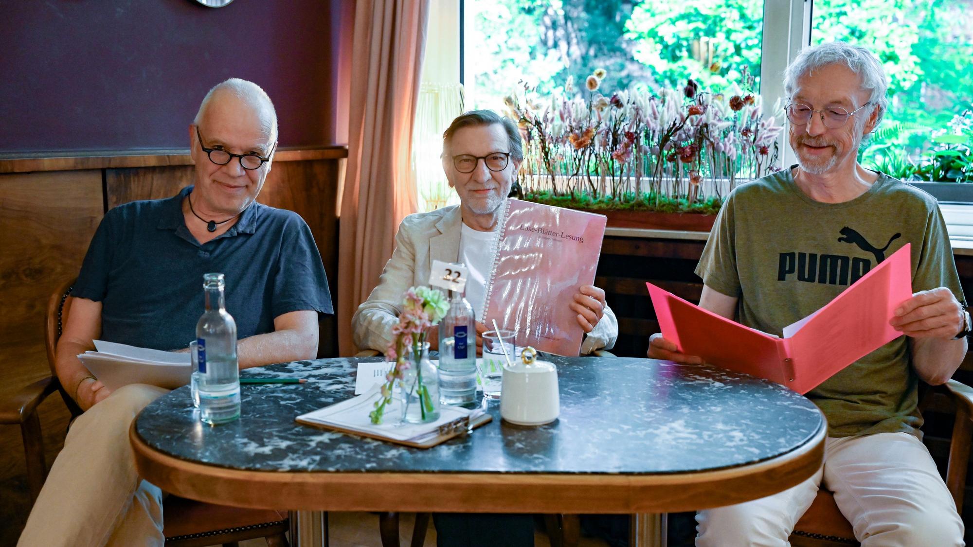 Drei Männer sitzen mit ihren Texten an einem Tisch im Café Osterspey in Sülz.