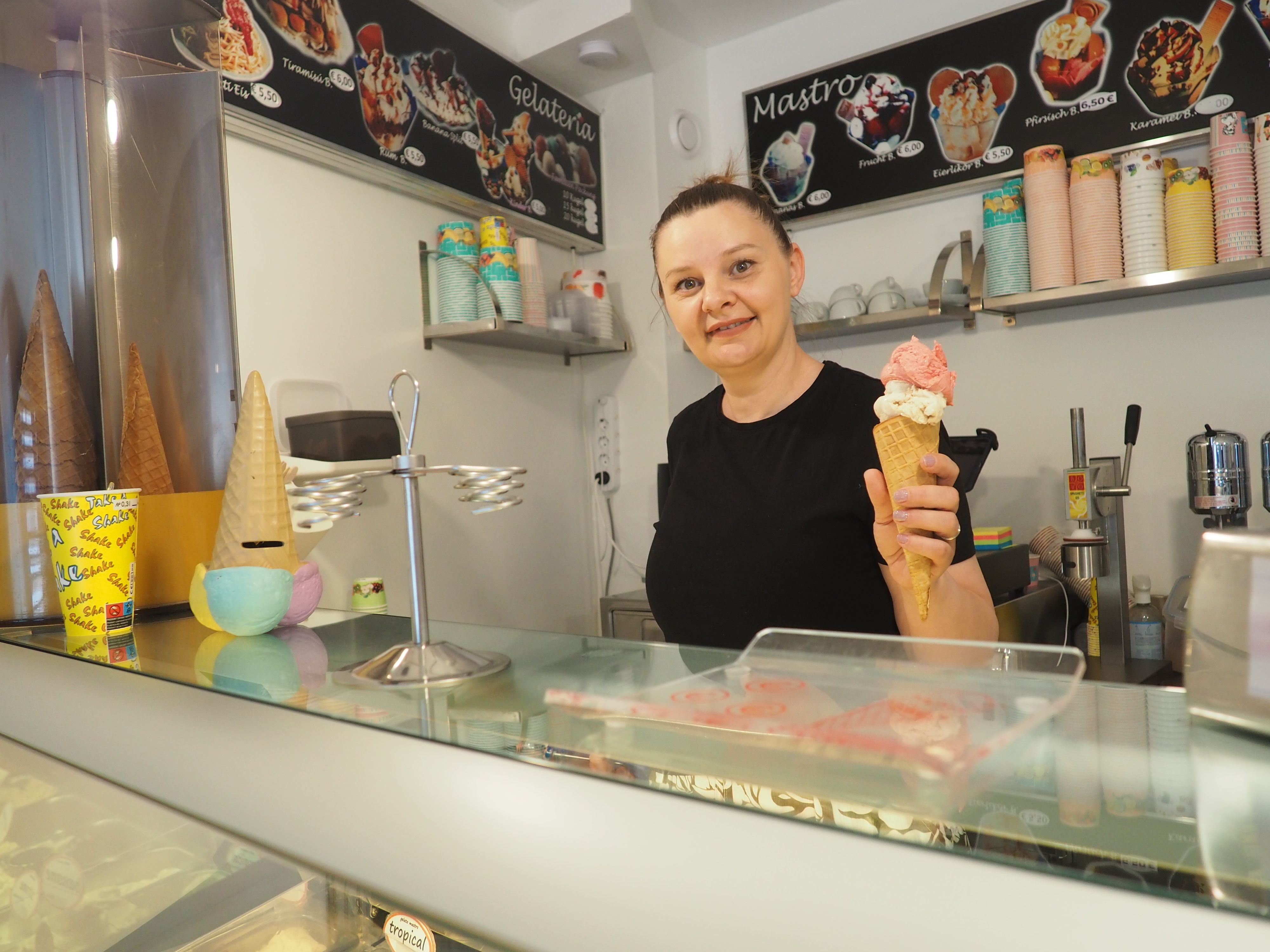 Daniela Pop steht hinter der Theke ihrer Eisdiele und hält ein Hörnchen mit Eiskugeln in der Hand.