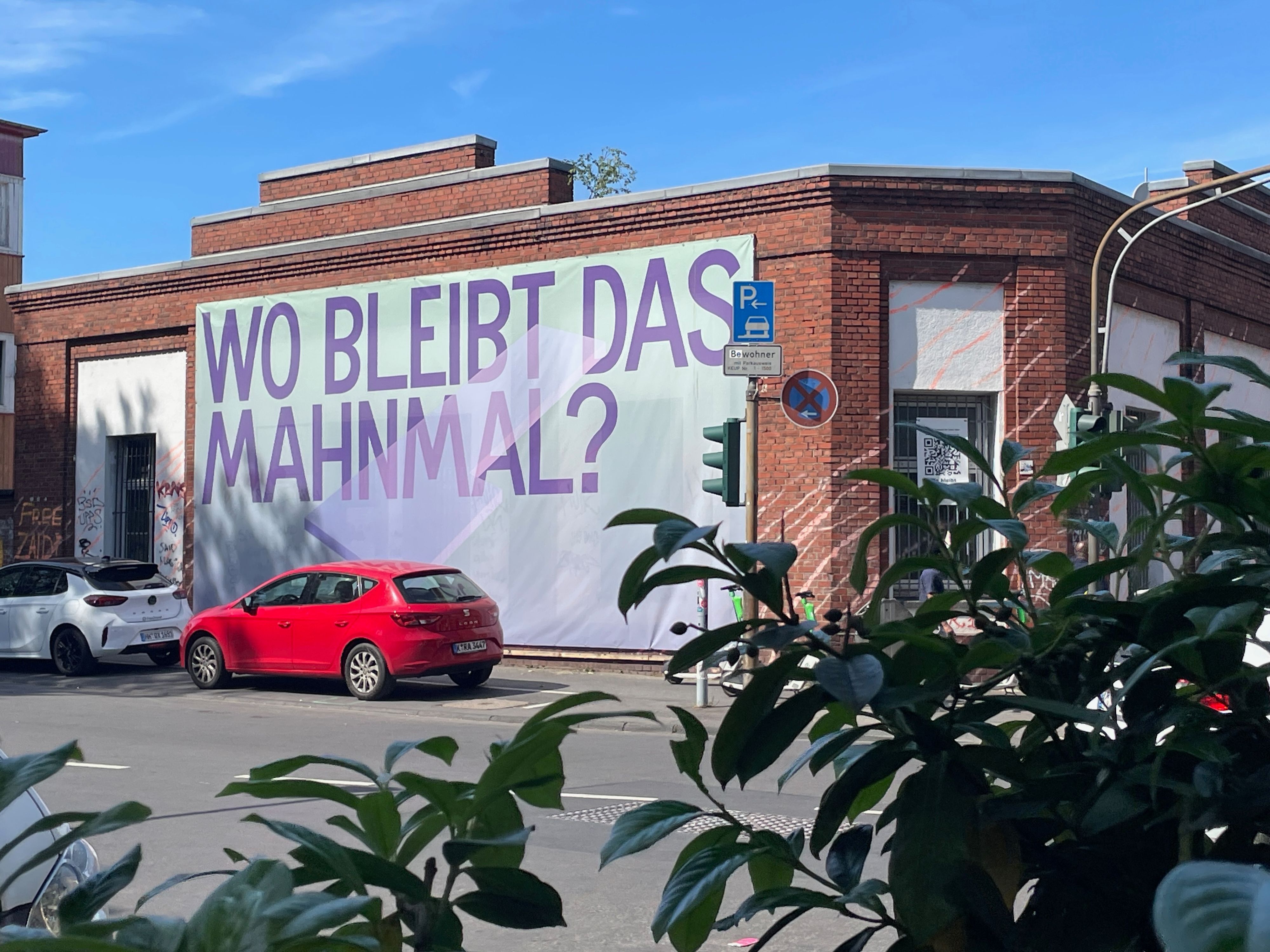 An der Backsteinfassade an einer Häuserecke hängt ein riesiges Banner: Wo bleibt das Mahnmal?