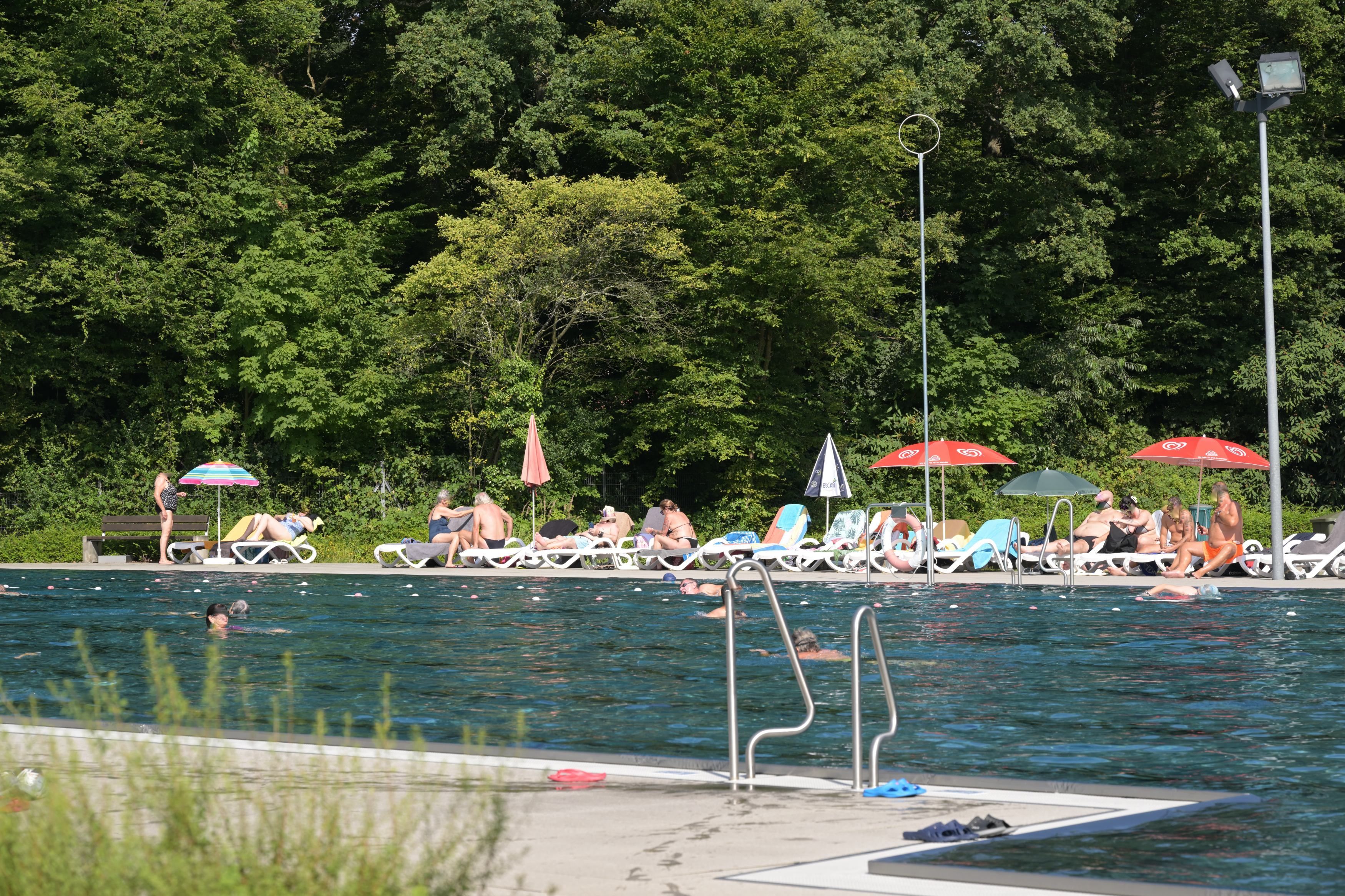 Im Vordergrund ist das Schwimmerbecken, im Hintergrund liegen Leute auf Liegen.
