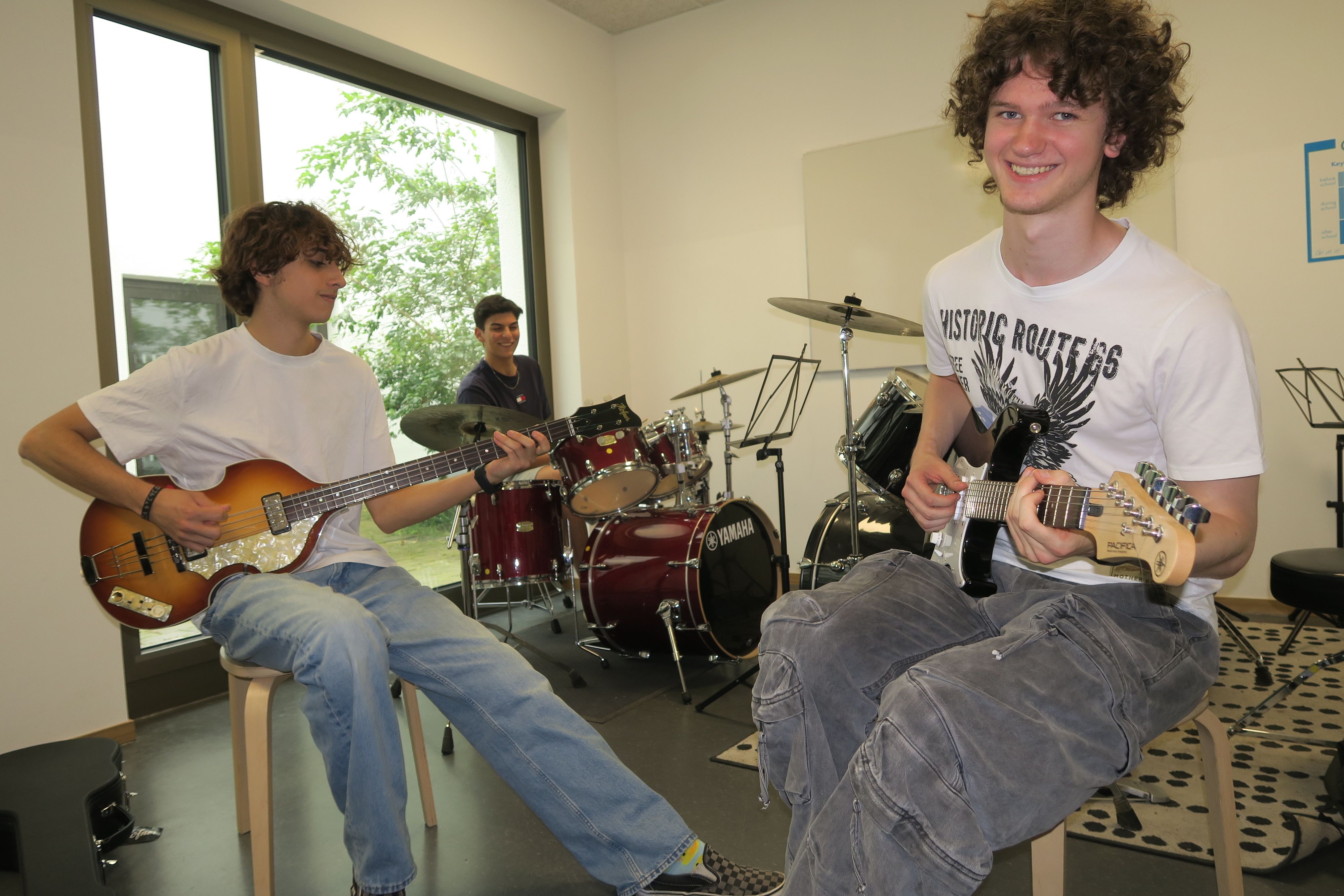 Drei junge Männer sitzen mit ihren Instrumenten in einem Proberaum.